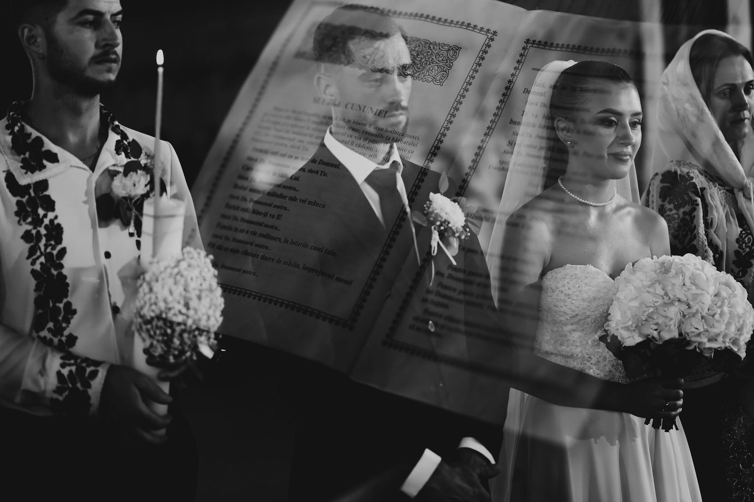 Black and white wedding ceremony photo of couple holding candles beneath a ceremonial cloth.