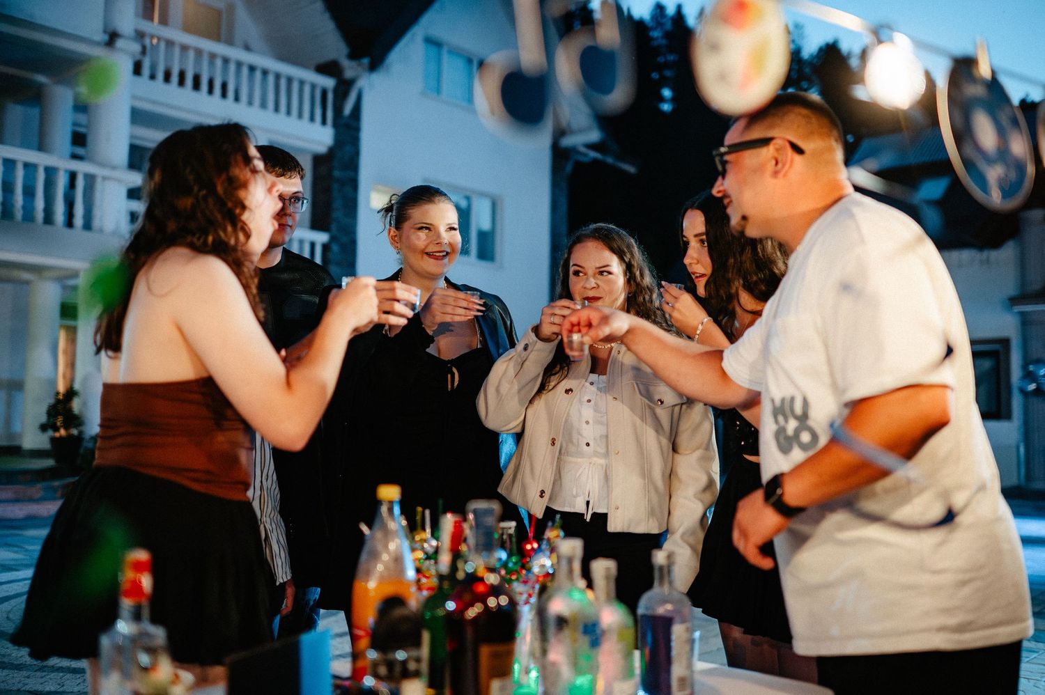Group of friends toasting drinks together at an outdoor evening party gathering.