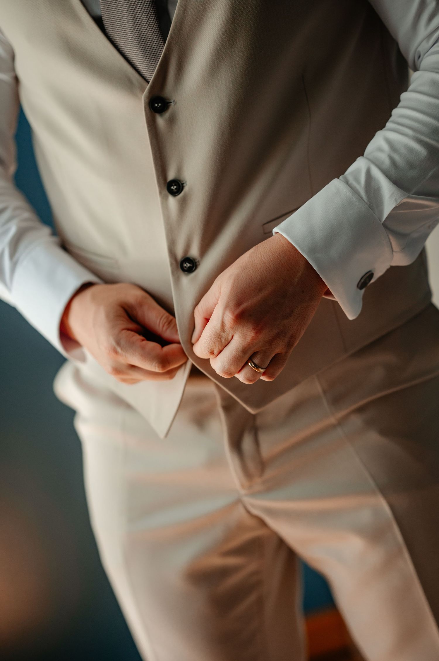 Groom fastening vest buttons wearing wedding ring close-up detail shot.