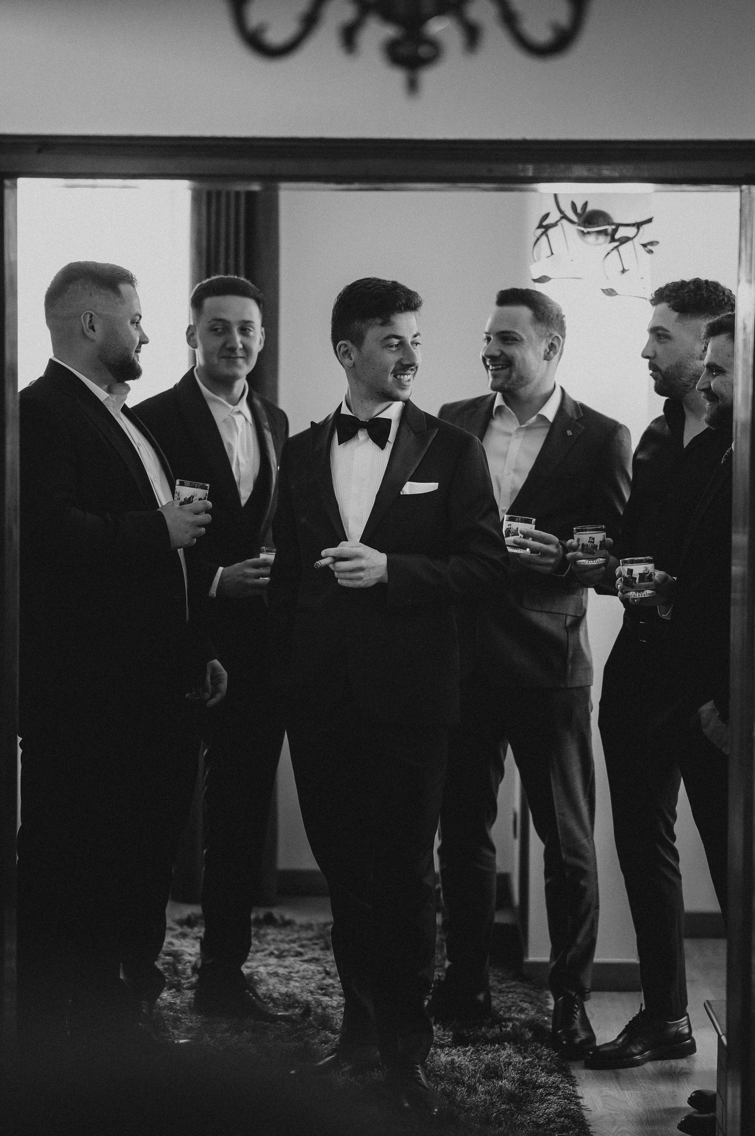 Black and white photo of groom and groomsmen socializing with drinks.
