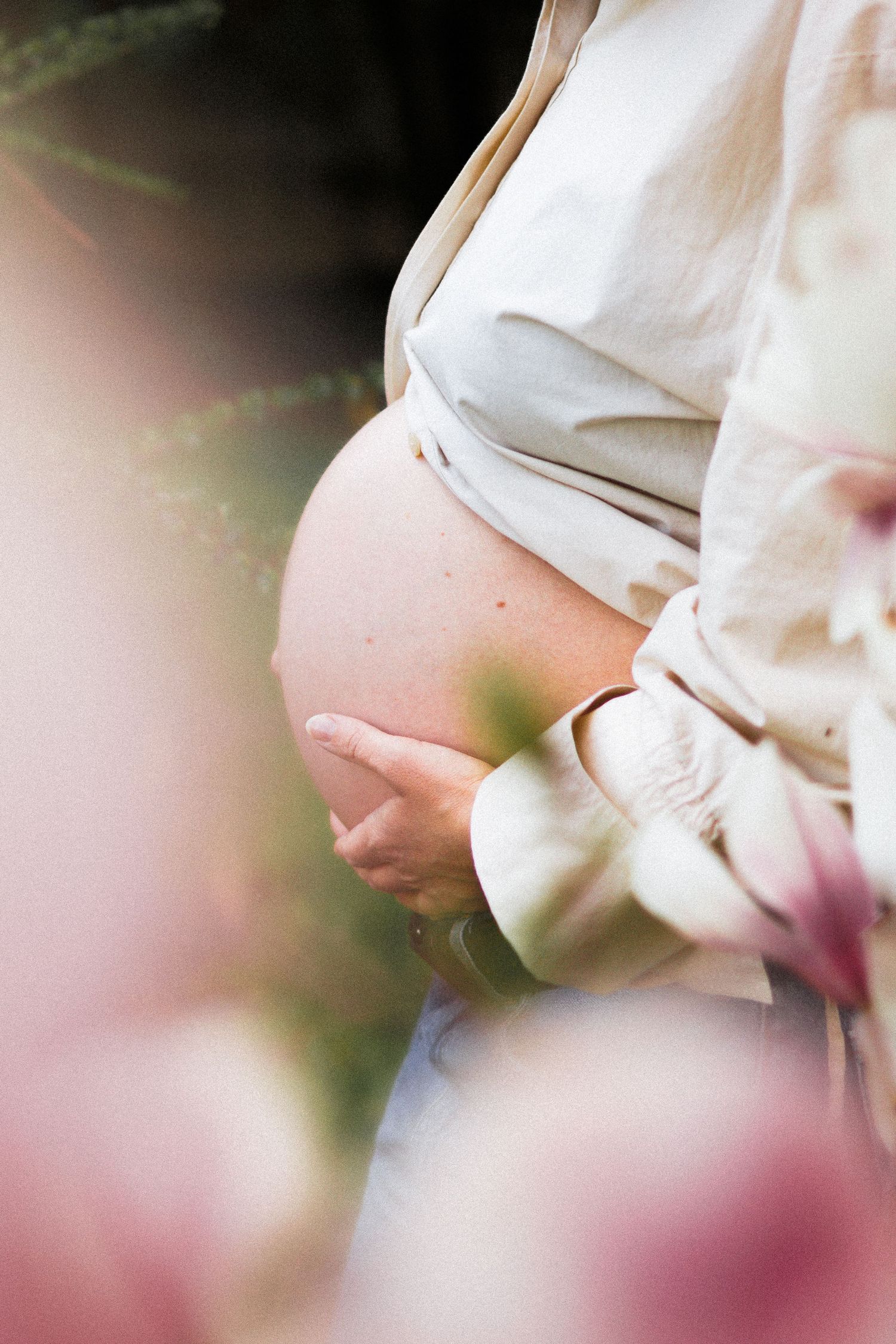 Close-up of pregnant woman in white shirt gently holding bare baby bump outdoors.