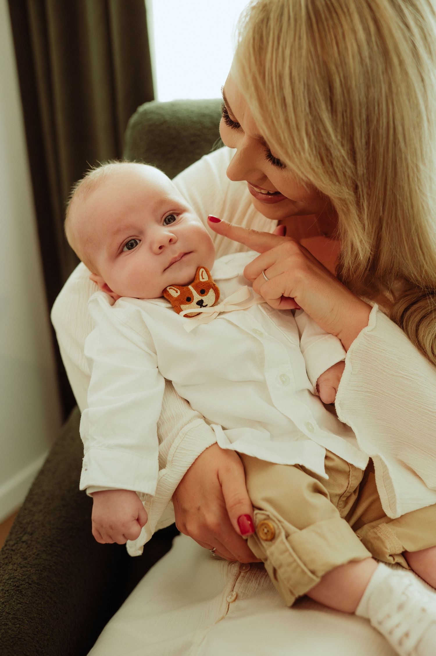Blonde mother smiling at adorable newborn baby wearing white outfit with corgi embroidery.