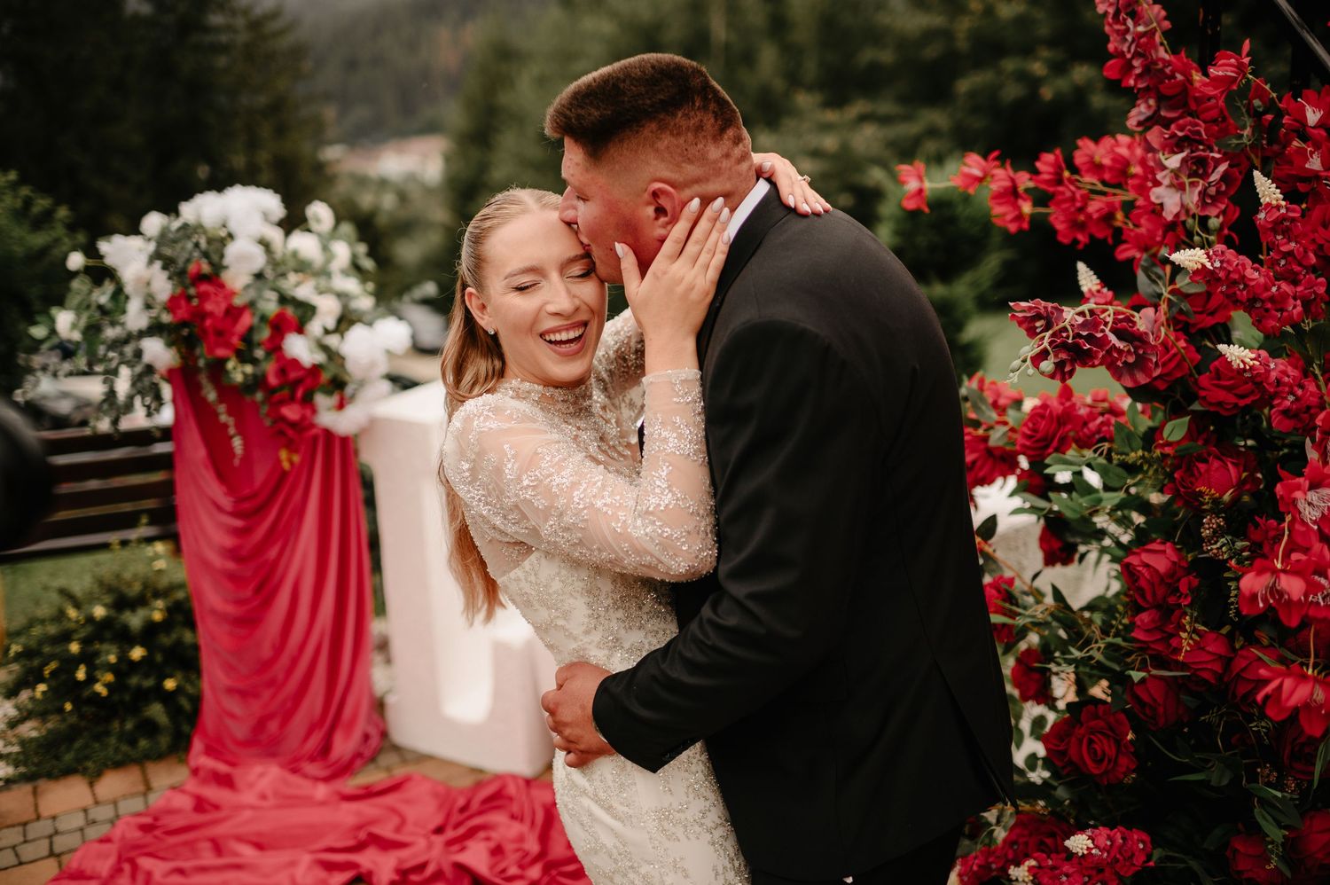 Joyful bride and groom sharing romantic moment at outdoor wedding ceremony with red rose arch.