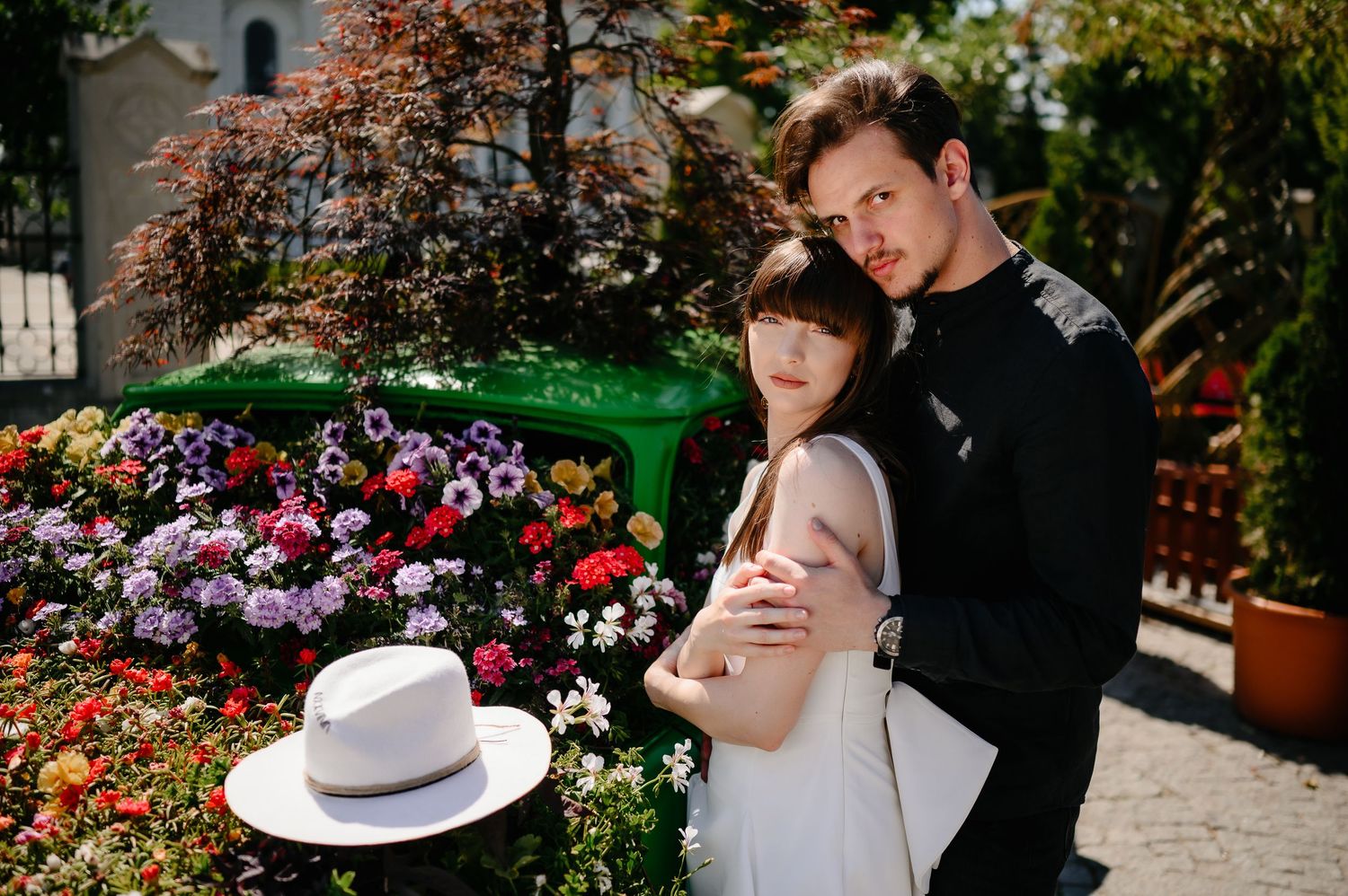 Romantic couple embracing in a colorful flower garden, woman in white dress, man in black shirt.
