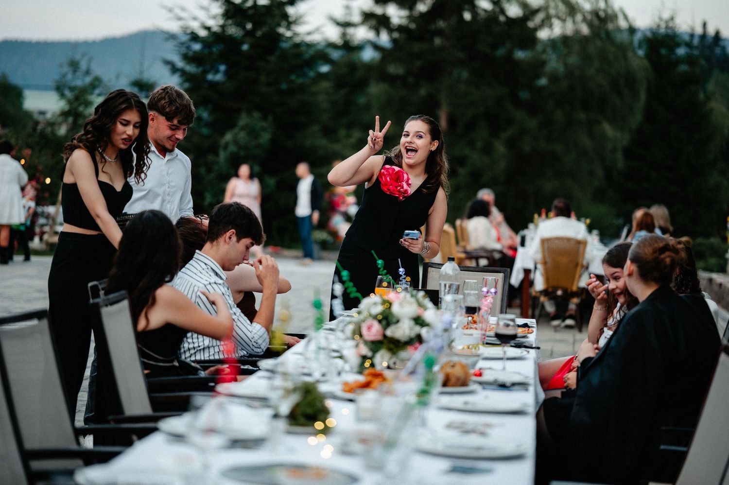 Young people gathered around a long decorated dinner table at an outdoor evening event.