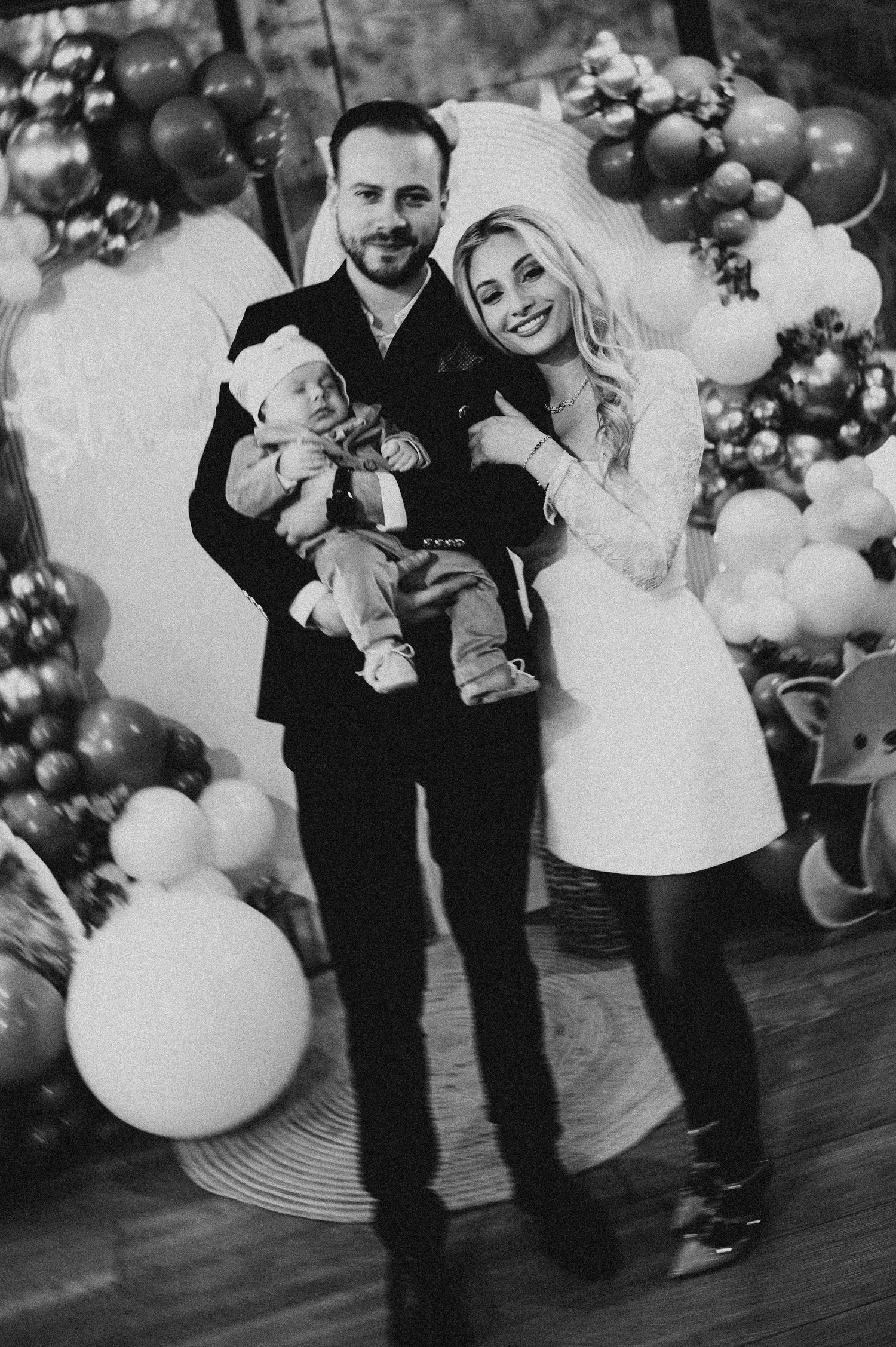 Black and white photo of proud parents holding their newborn baby at a woodland-themed christening party.