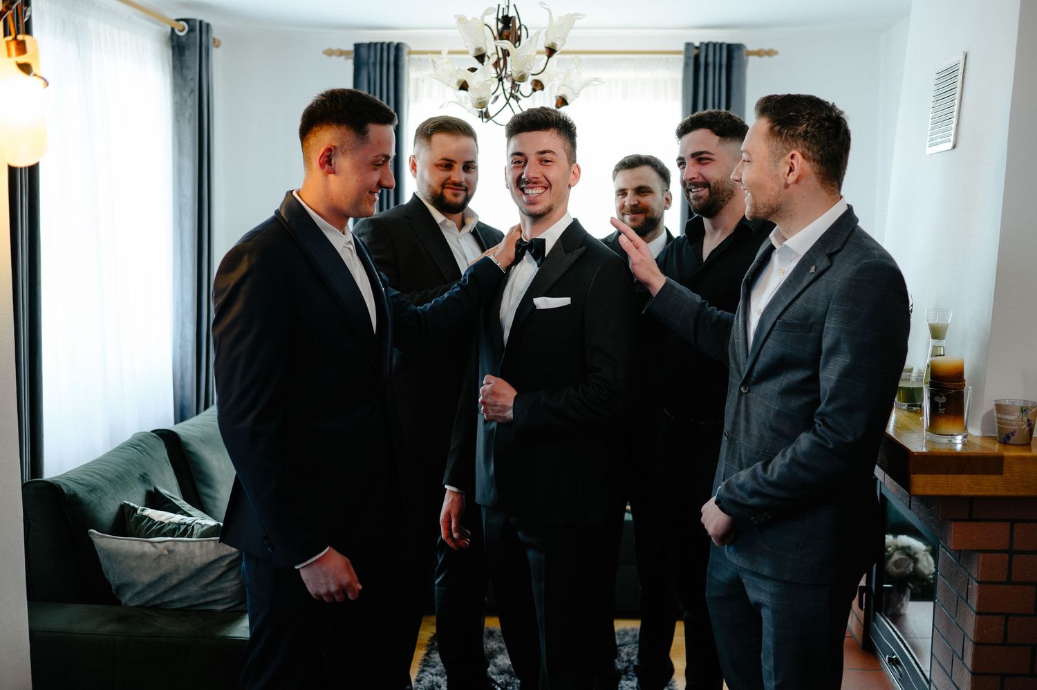 Groom and groomsmen laughing together while helping adjust bow tie before wedding ceremony.