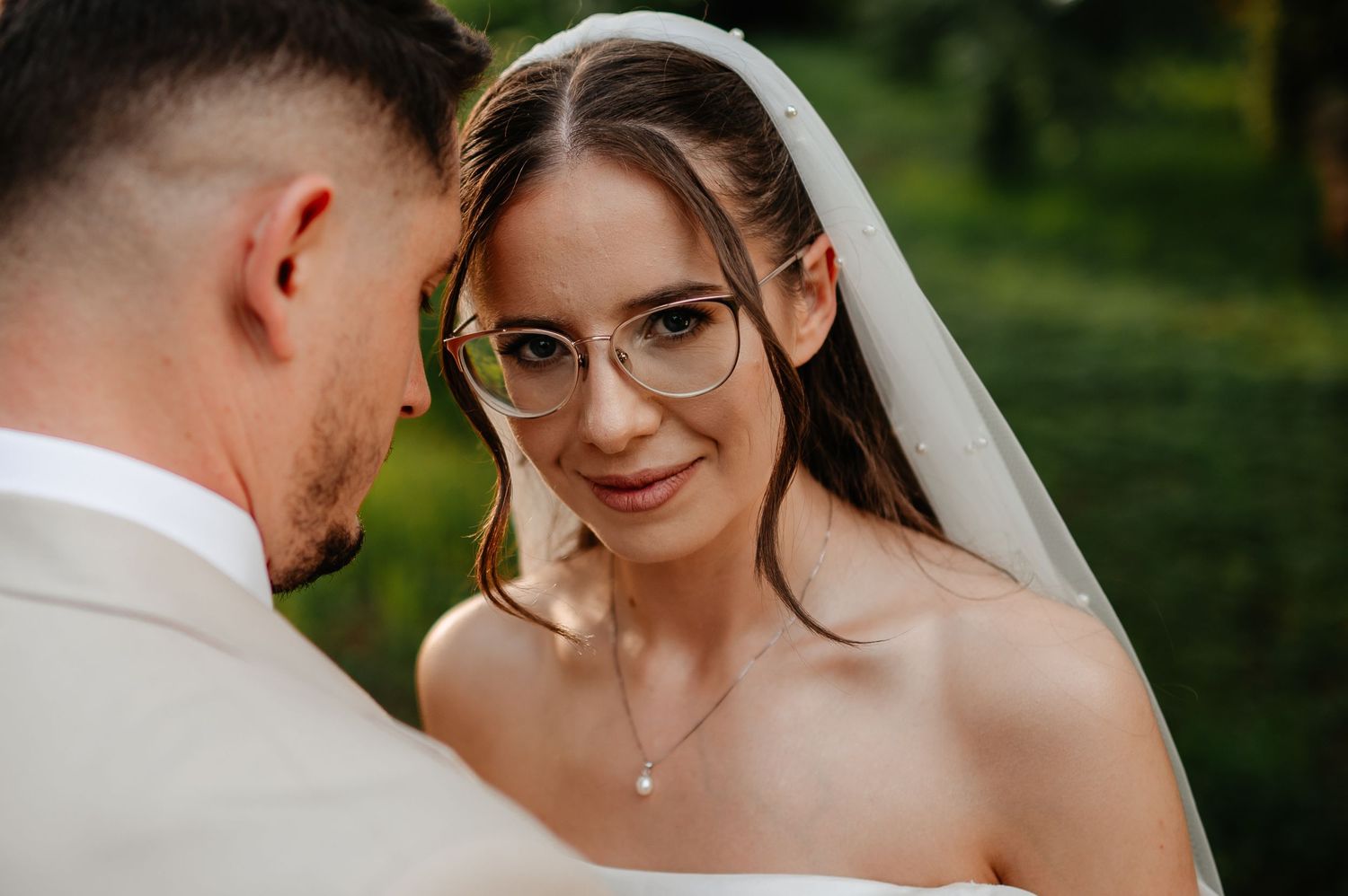 Close-up of smiling bride wearing glasses and veil with pearl necklace on wedding day.