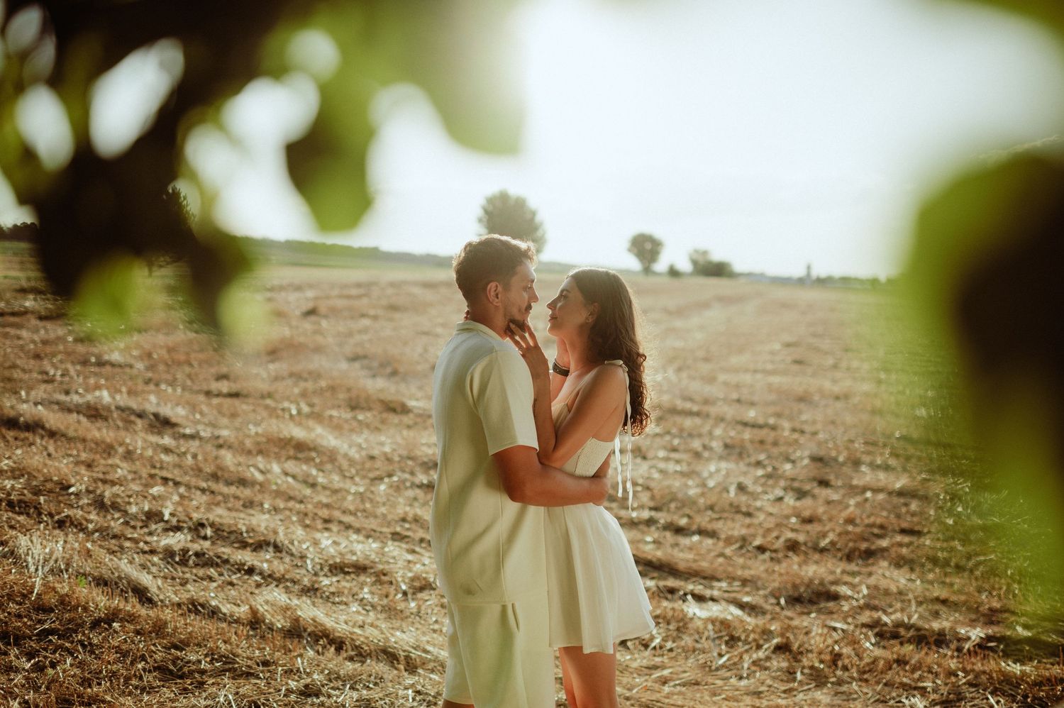 Couple sharing a tender moment in a golden harvested field.