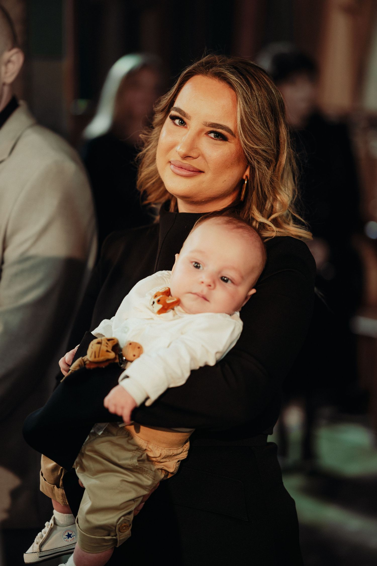 Young mother in black dress holding her infant baby at a baptism ceremony in a church.