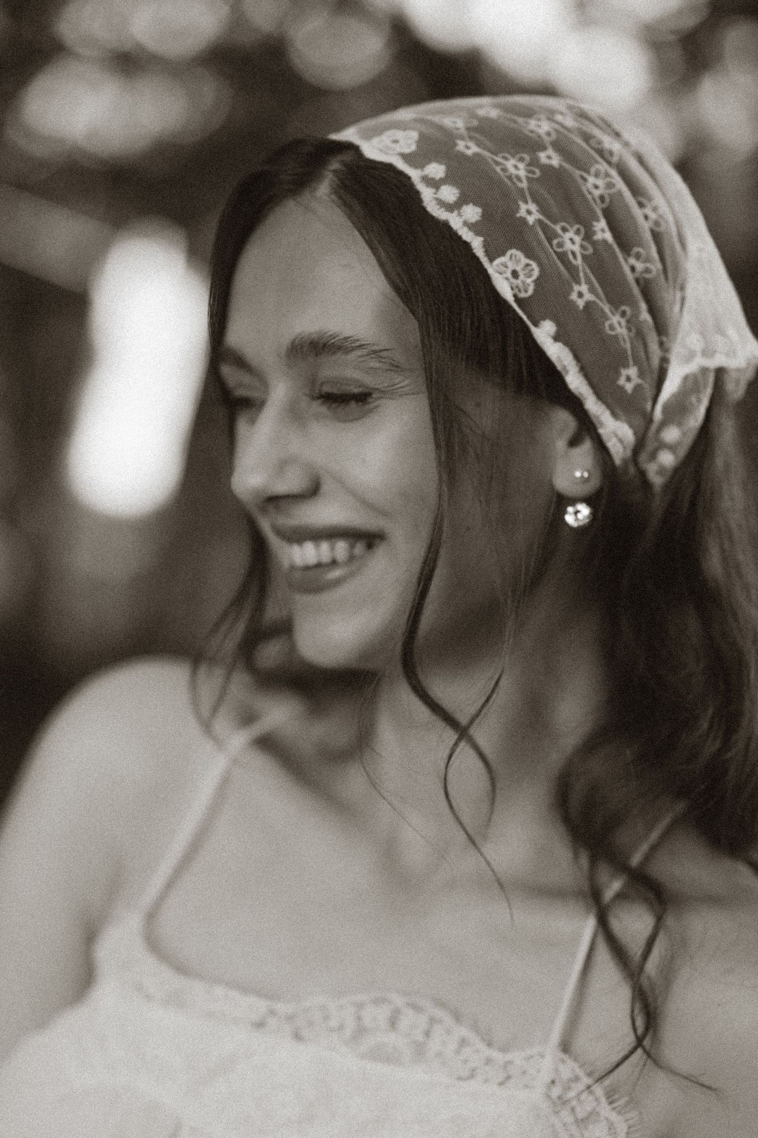 Black and white portrait of a smiling young woman wearing a lace headscarf and pearl earrings.