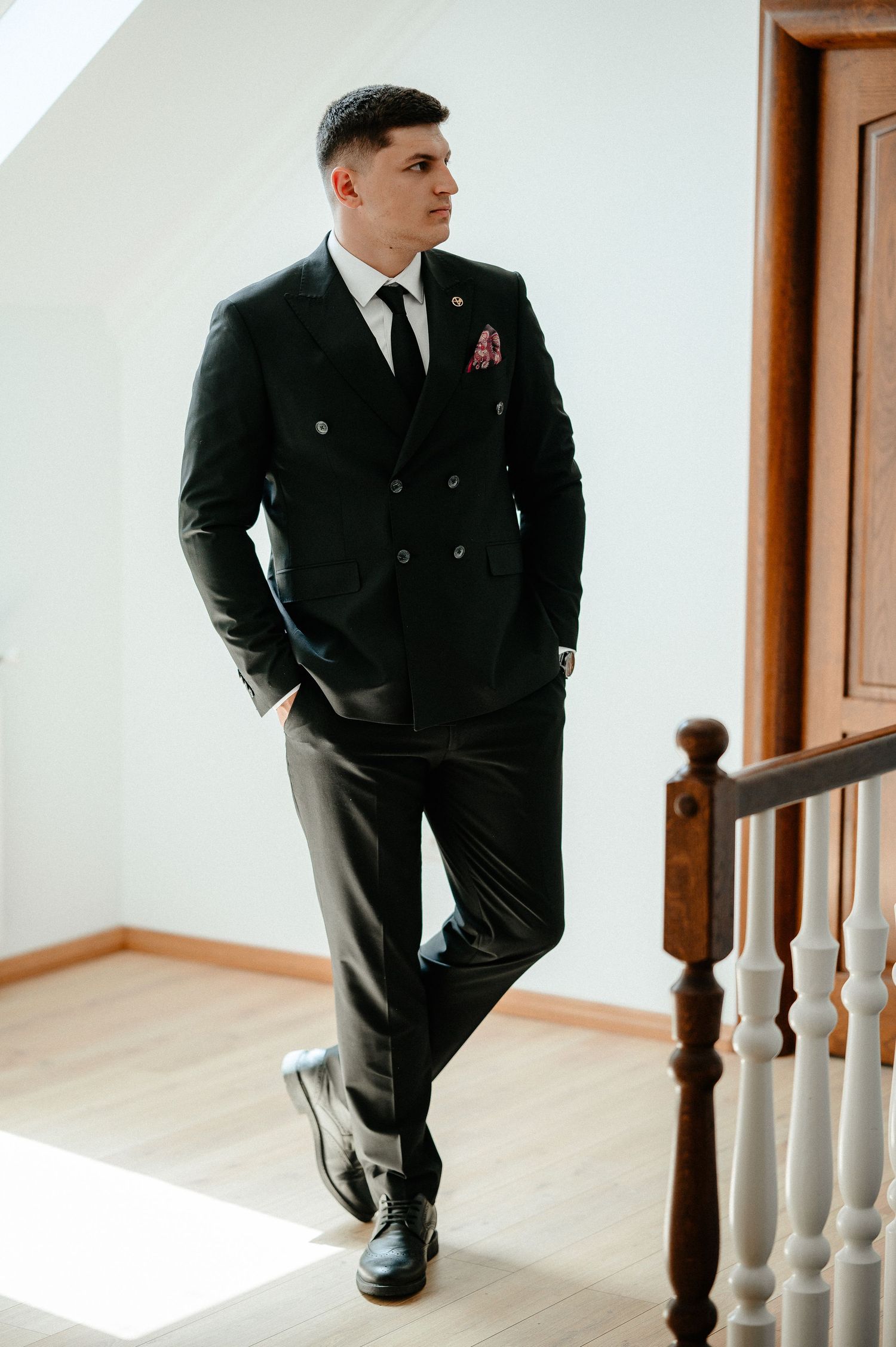 Groom in black double-breasted suit with pink pocket square posing on staircase.
