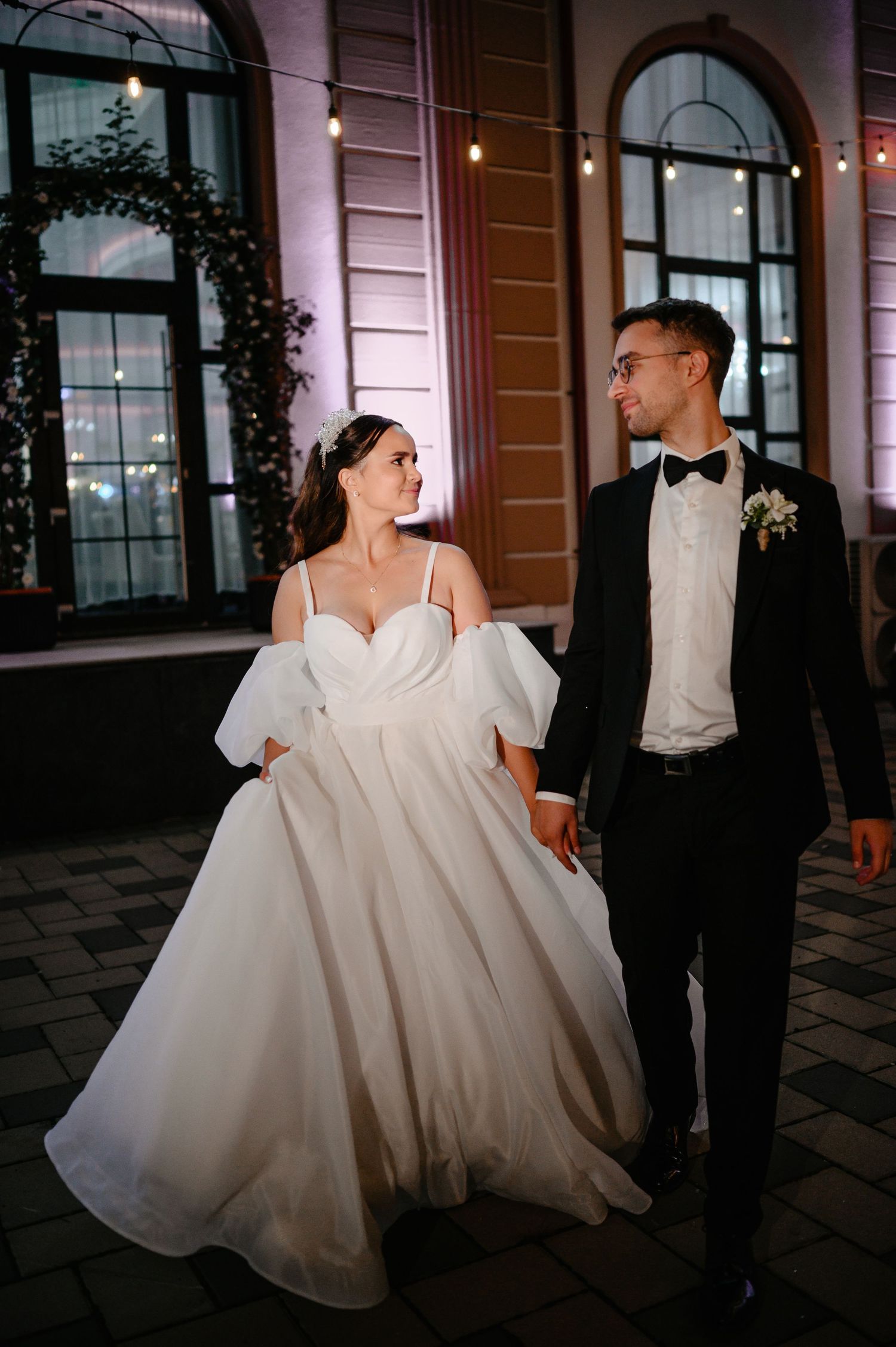 Wedding couple holding hands outdoors at night, bride in ballgown, groom in tuxedo.