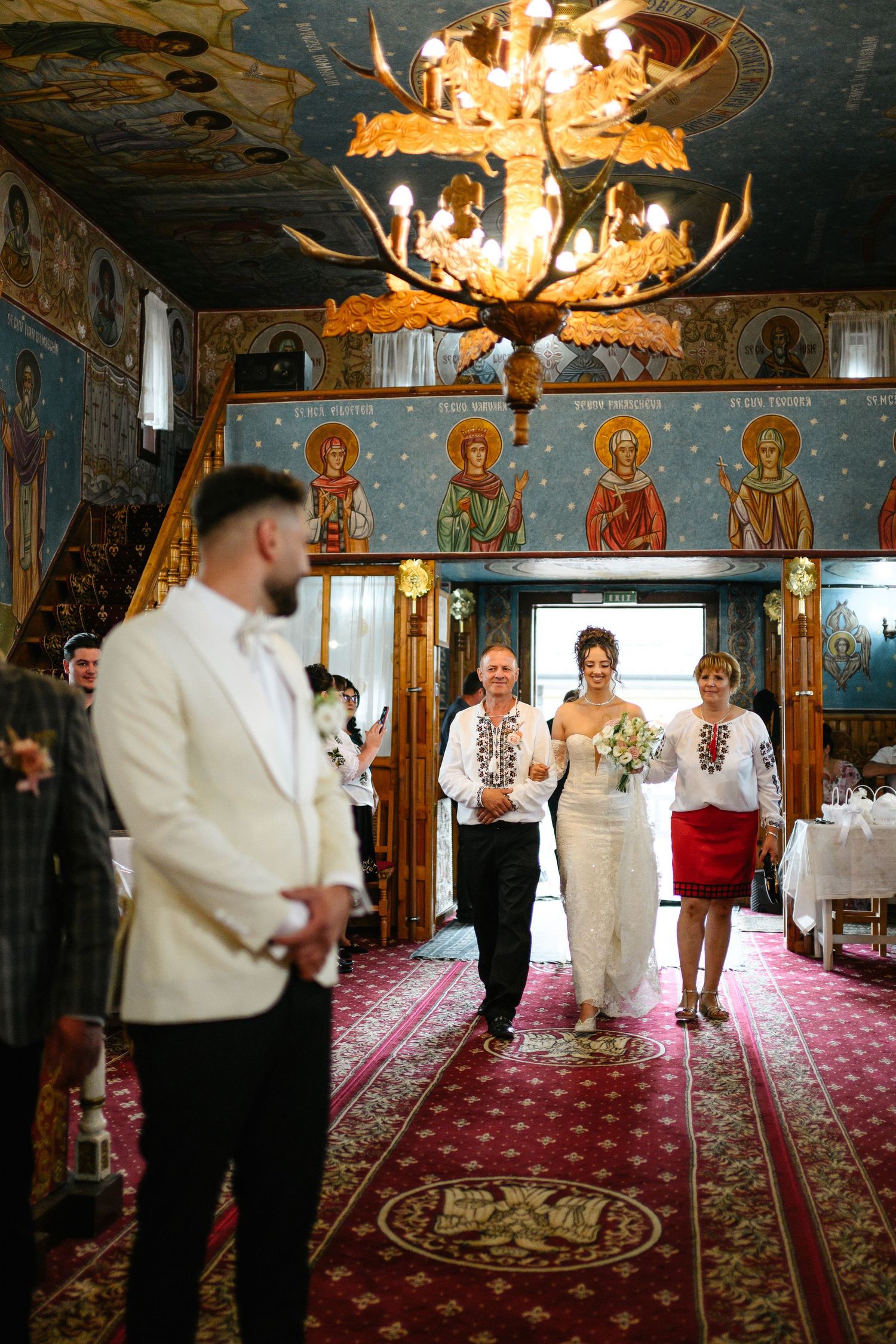 Wedding ceremony in ornate church with bride walking down aisle in traditional embroidered dress.