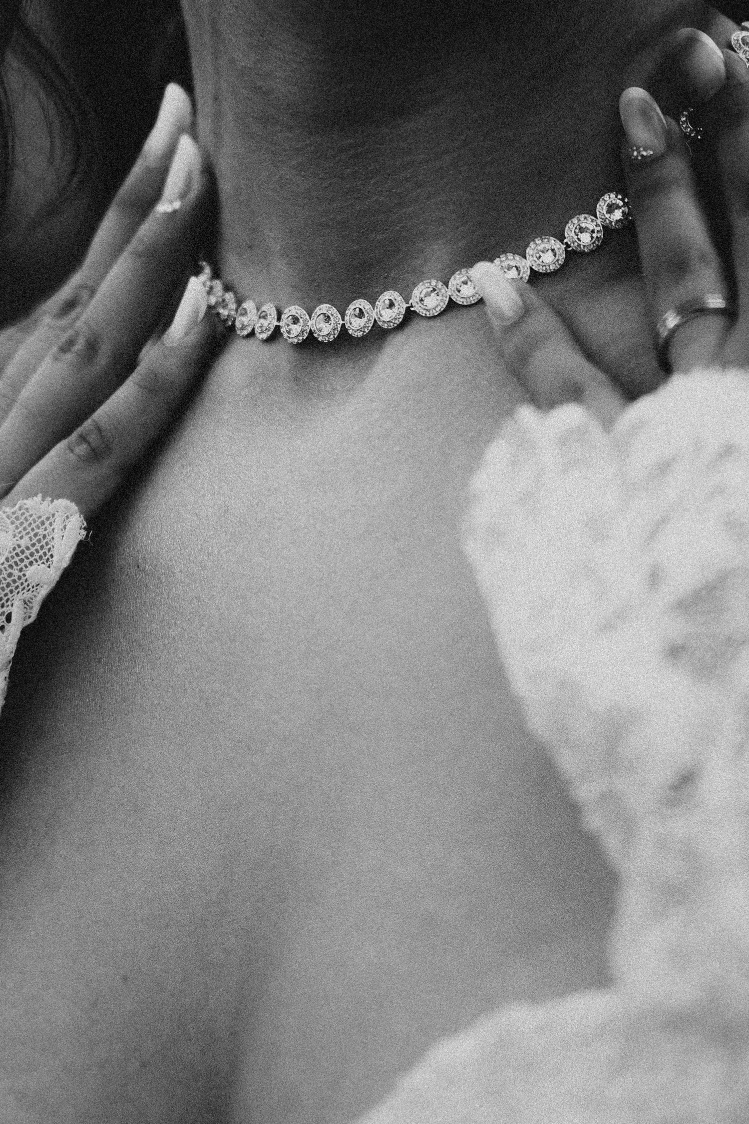 Close-up black and white photo of a bride wearing an elegant diamond choker necklace on her wedding day.