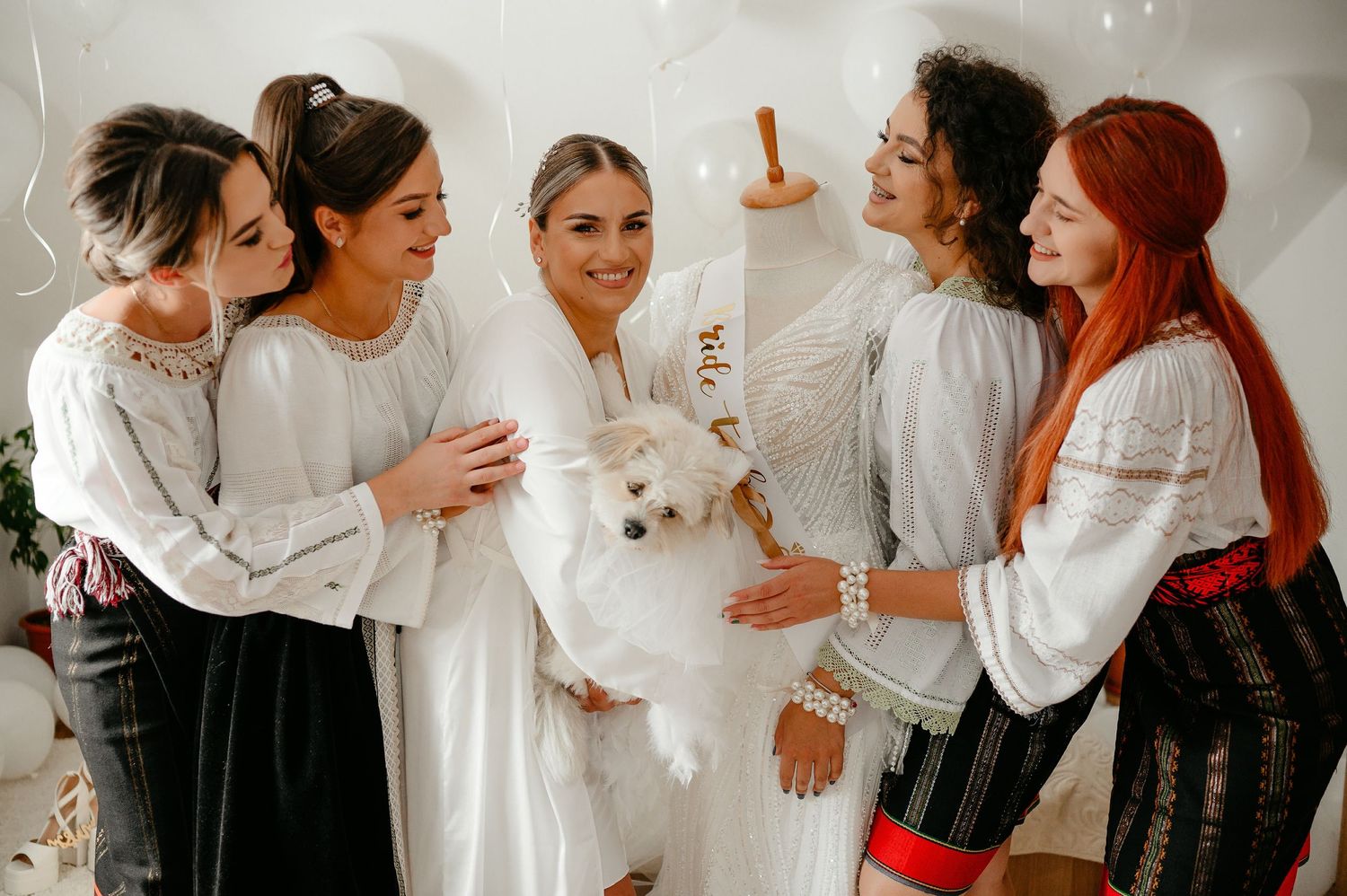 Bride in white dress holding small white dog surrounded by bridesmaids.