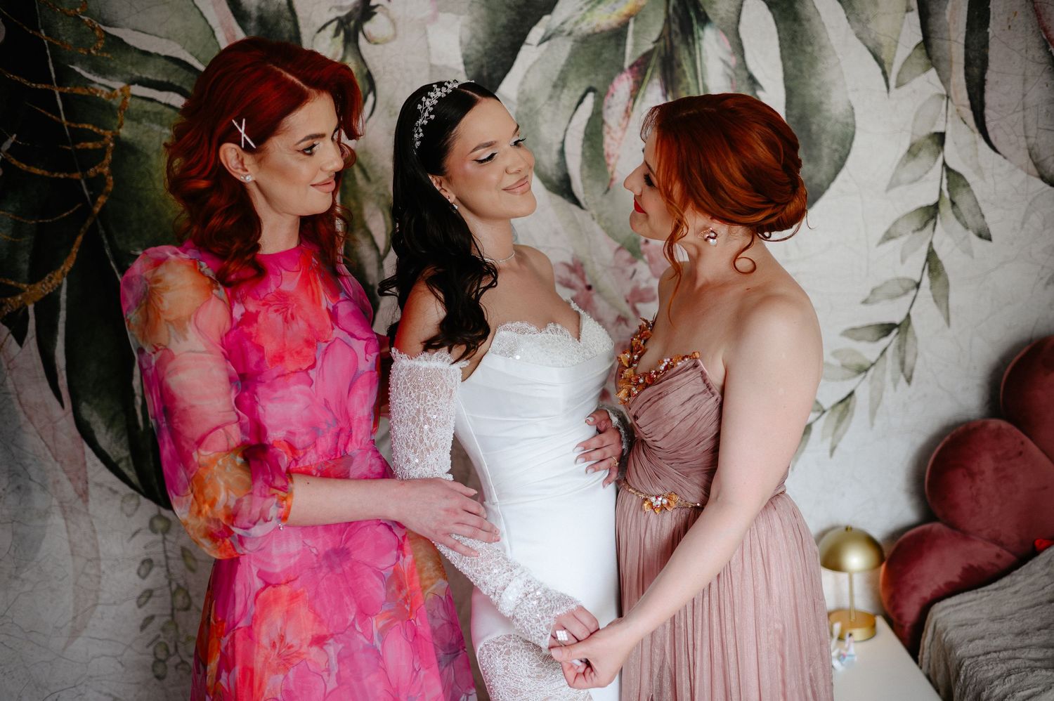 Bride in white wedding gown standing between two red-haired bridesmaids in colorful dresses holding hands.