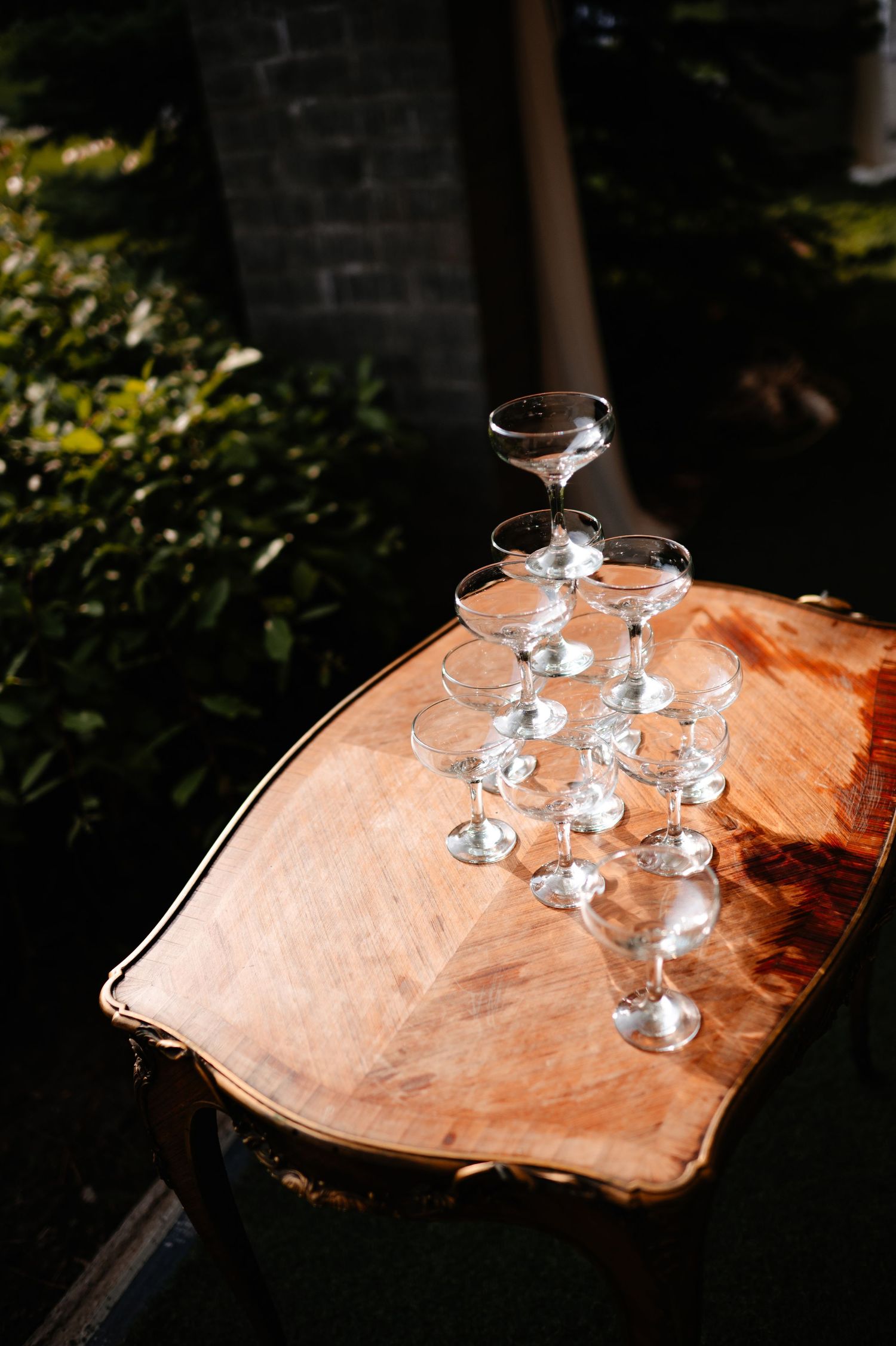 Elegant champagne coupe glasses arranged on a rustic wooden table outdoors in sunlight.