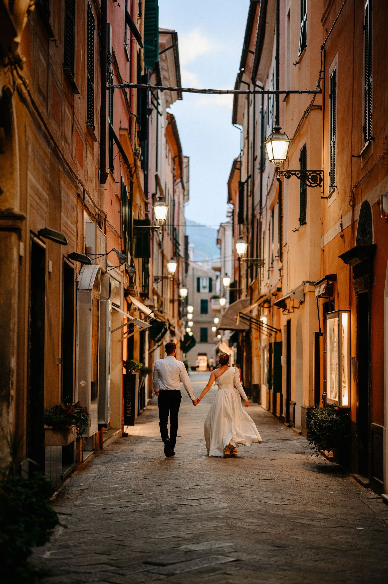 Newlyweds walking hand in hand through a charming narrow Italian alley at night.
