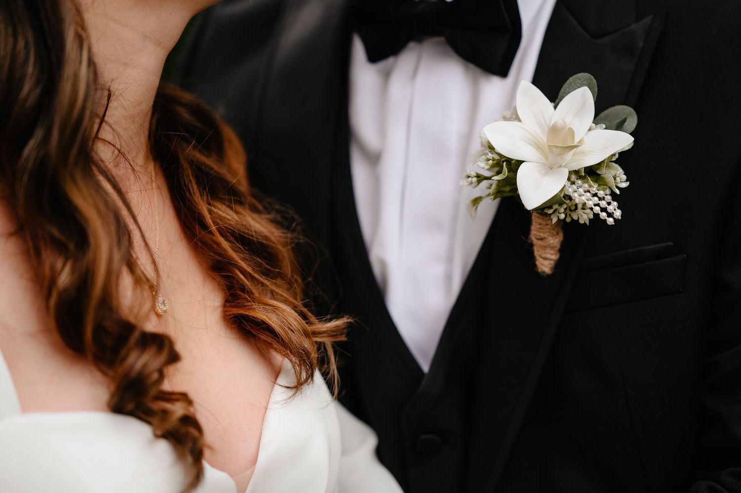 Close-up of grooms boutonniere with white magnolia flower on black tuxedo lapel.