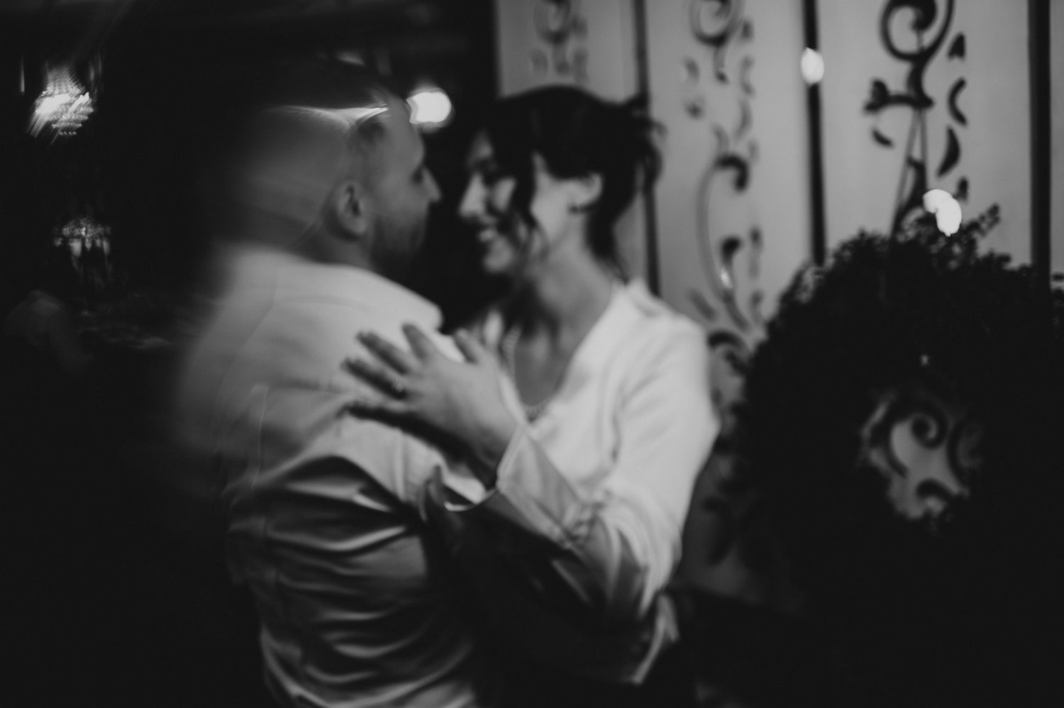 Black and white photo of a couple sharing a romantic dance at an elegant indoor celebration.