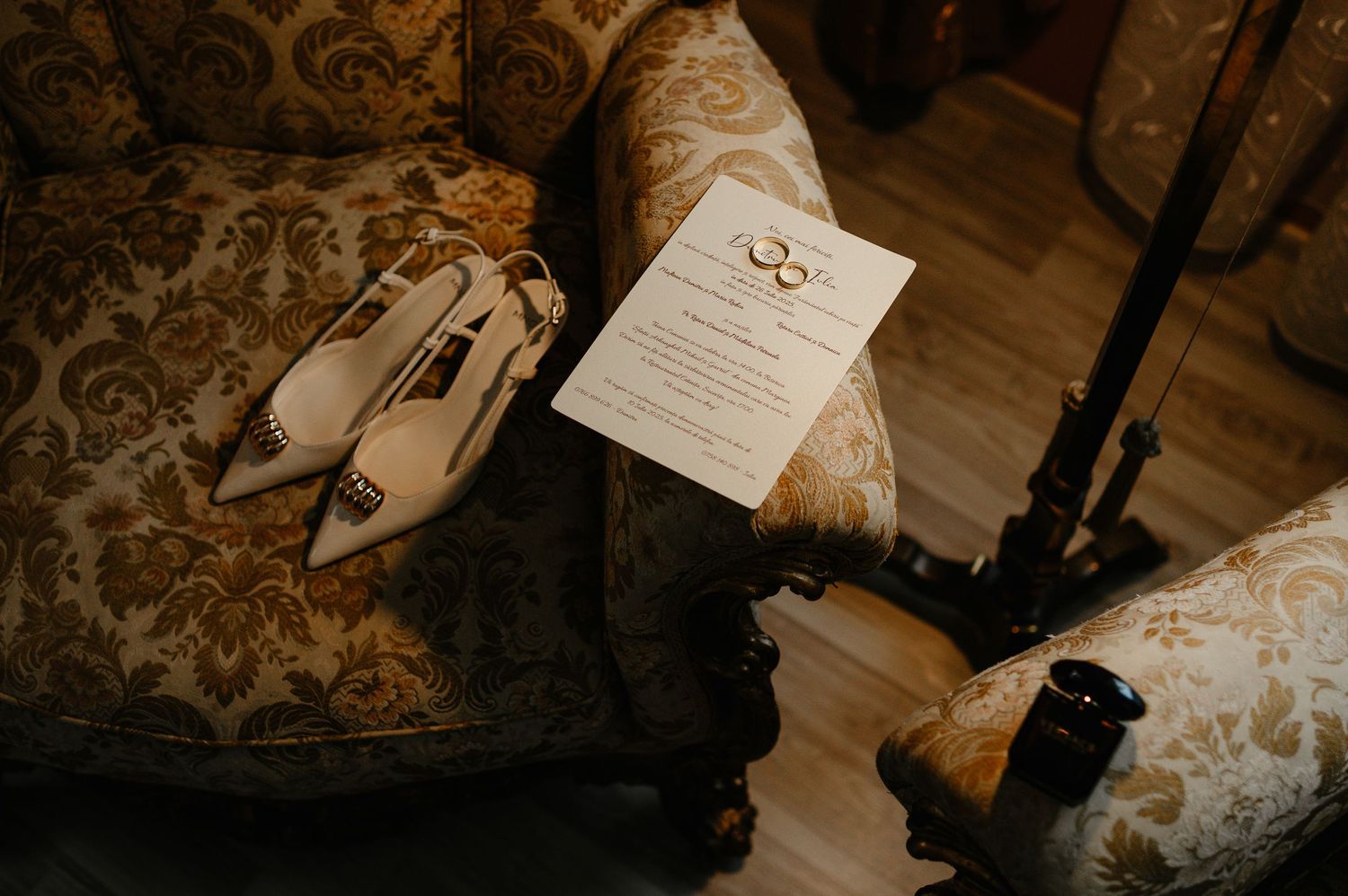 Elegant wedding flat lay with ivory heels, gold rings, and invitation on vintage floral armchair.