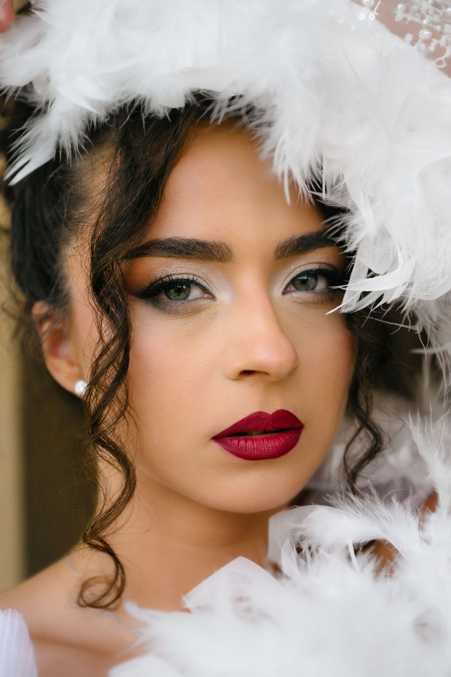 Woman with dramatic makeup, red lips, and white feathers framing her face in an elegant portrait.