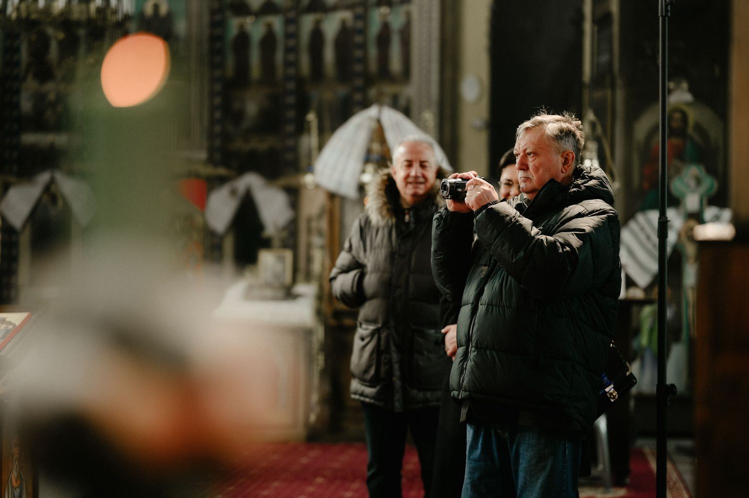 Two elderly people standing inside an ornate Orthodox church during a ceremony.