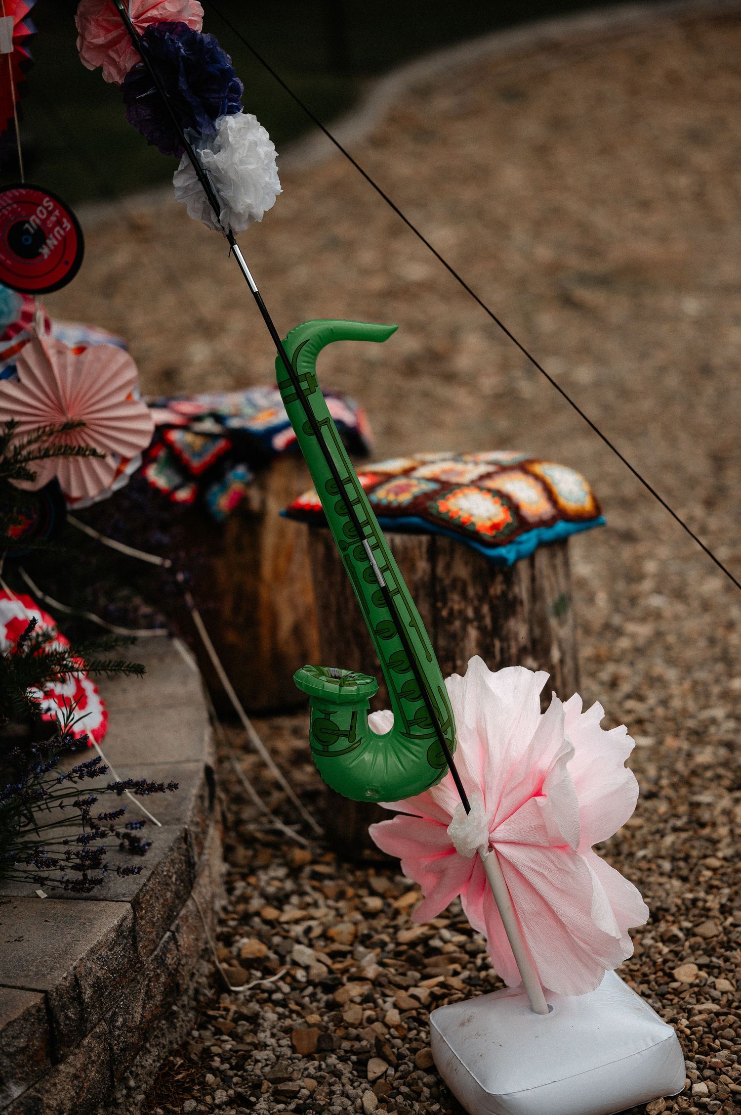 Green inflatable saxophone with pink paper flower decoration at an outdoor party with colorful paper fans.