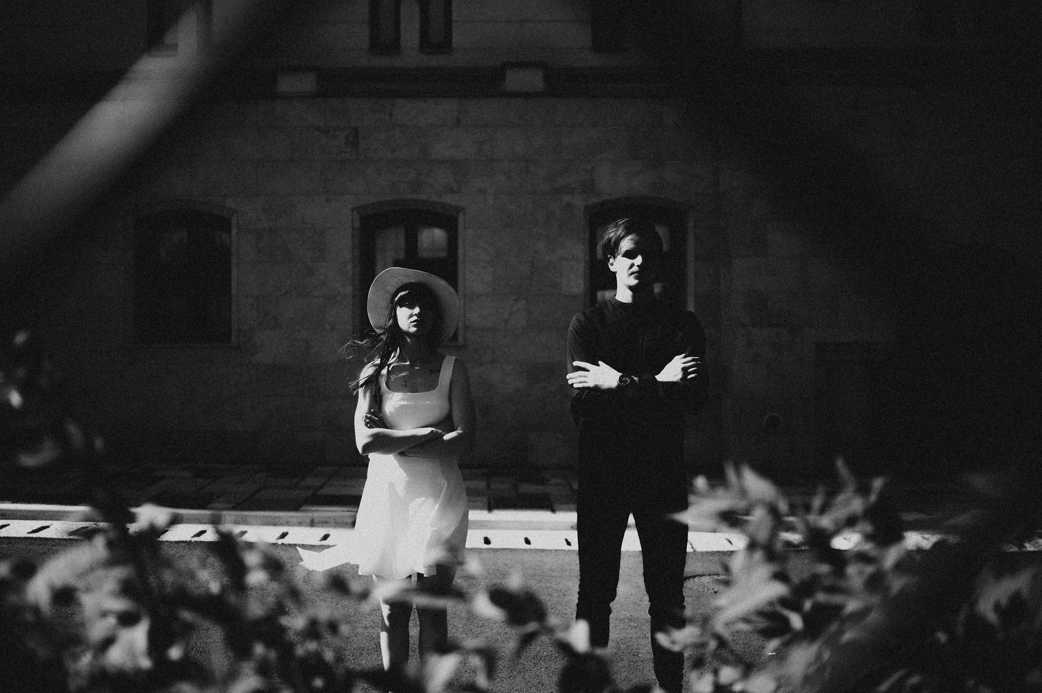 Black and white photo of a couple standing apart in front of a historic building.