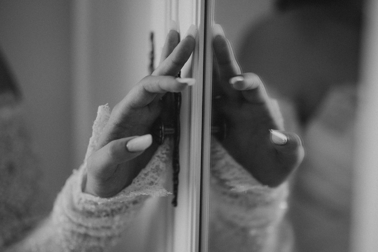 Black and white photo of hands with white nails touching a mirror reflection.