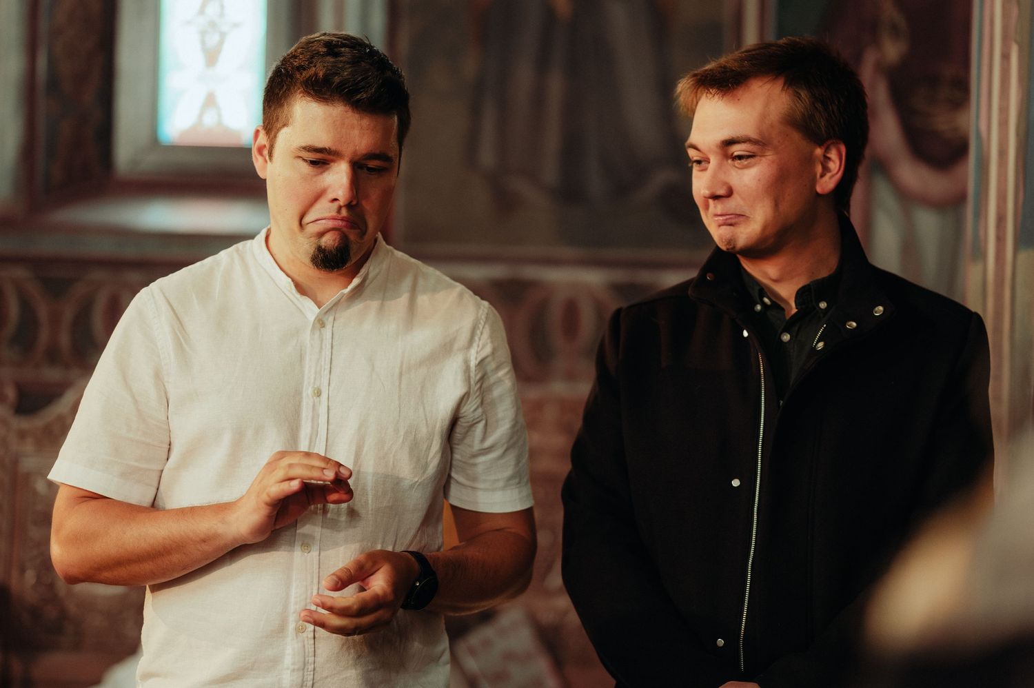 Two men standing together in a ornate interior, one in white shirt examining an object.