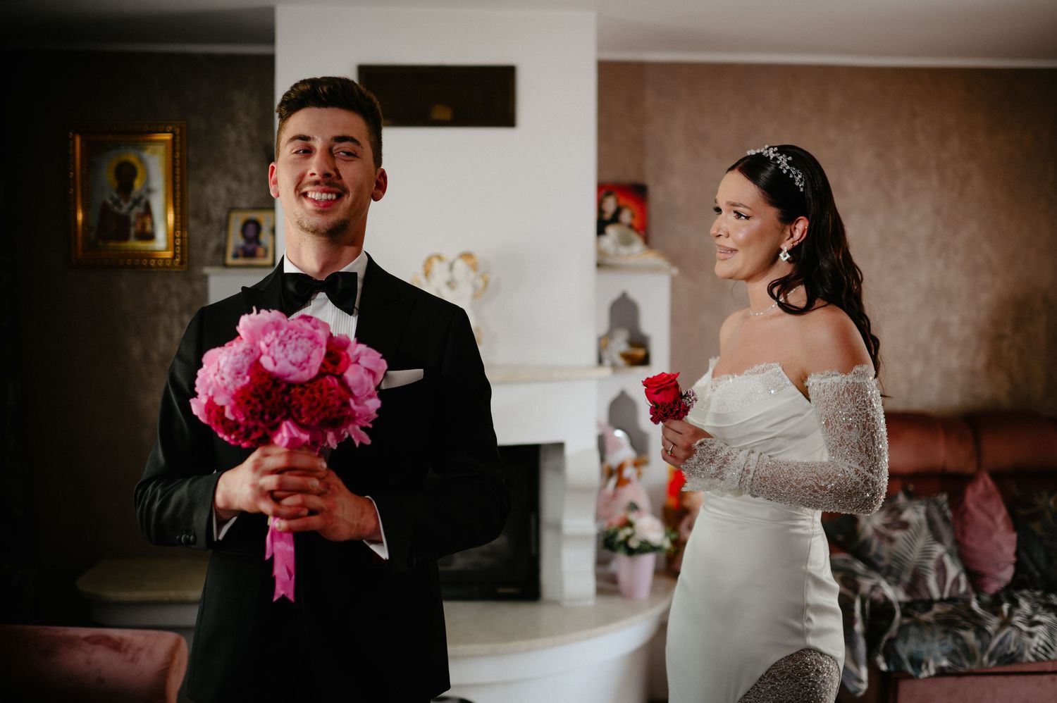Smiling groom holds vibrant pink peony bouquet during first look with bride in white gown.