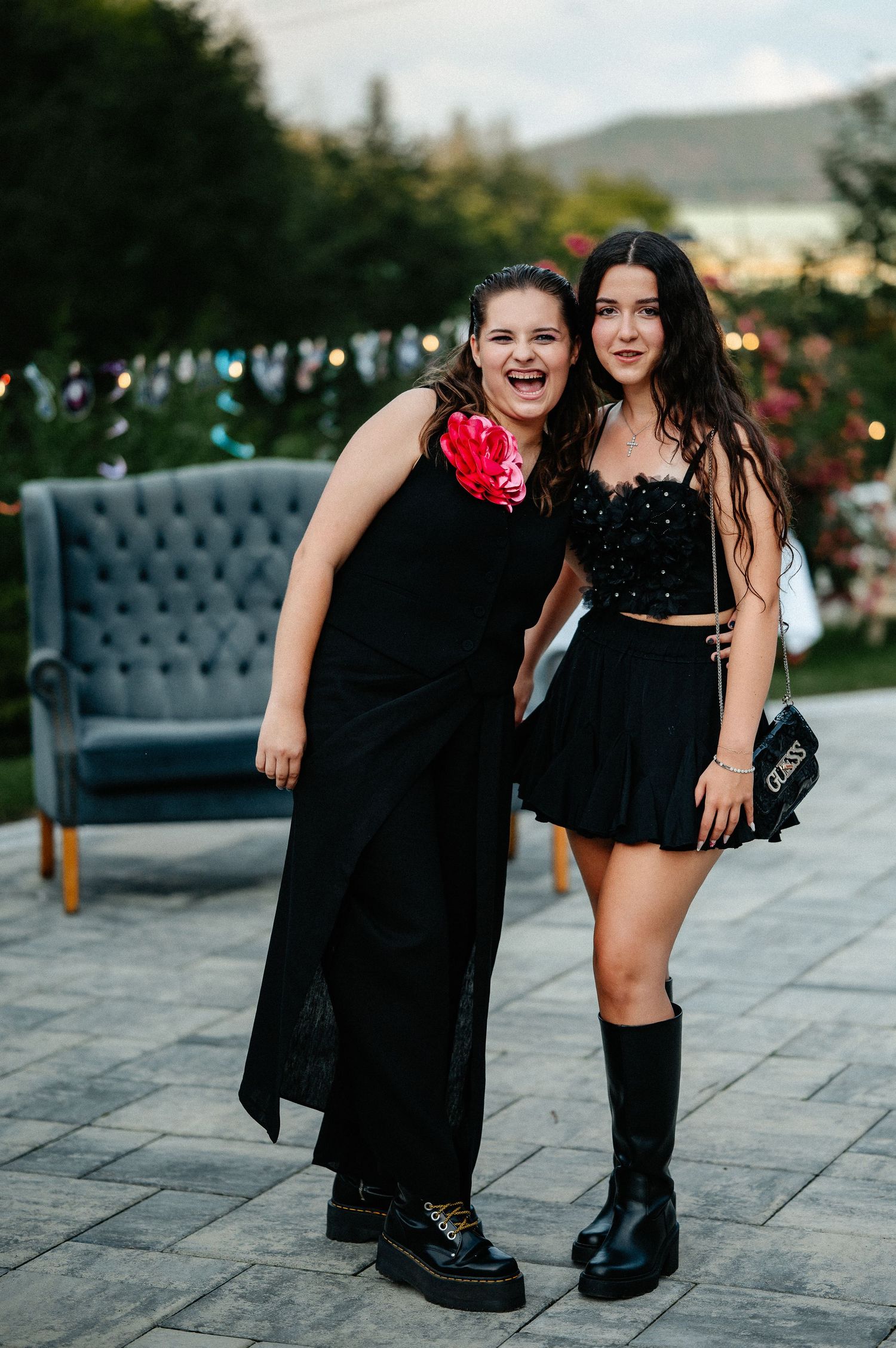 Two young women in black outfits smiling together at an outdoor garden party event.