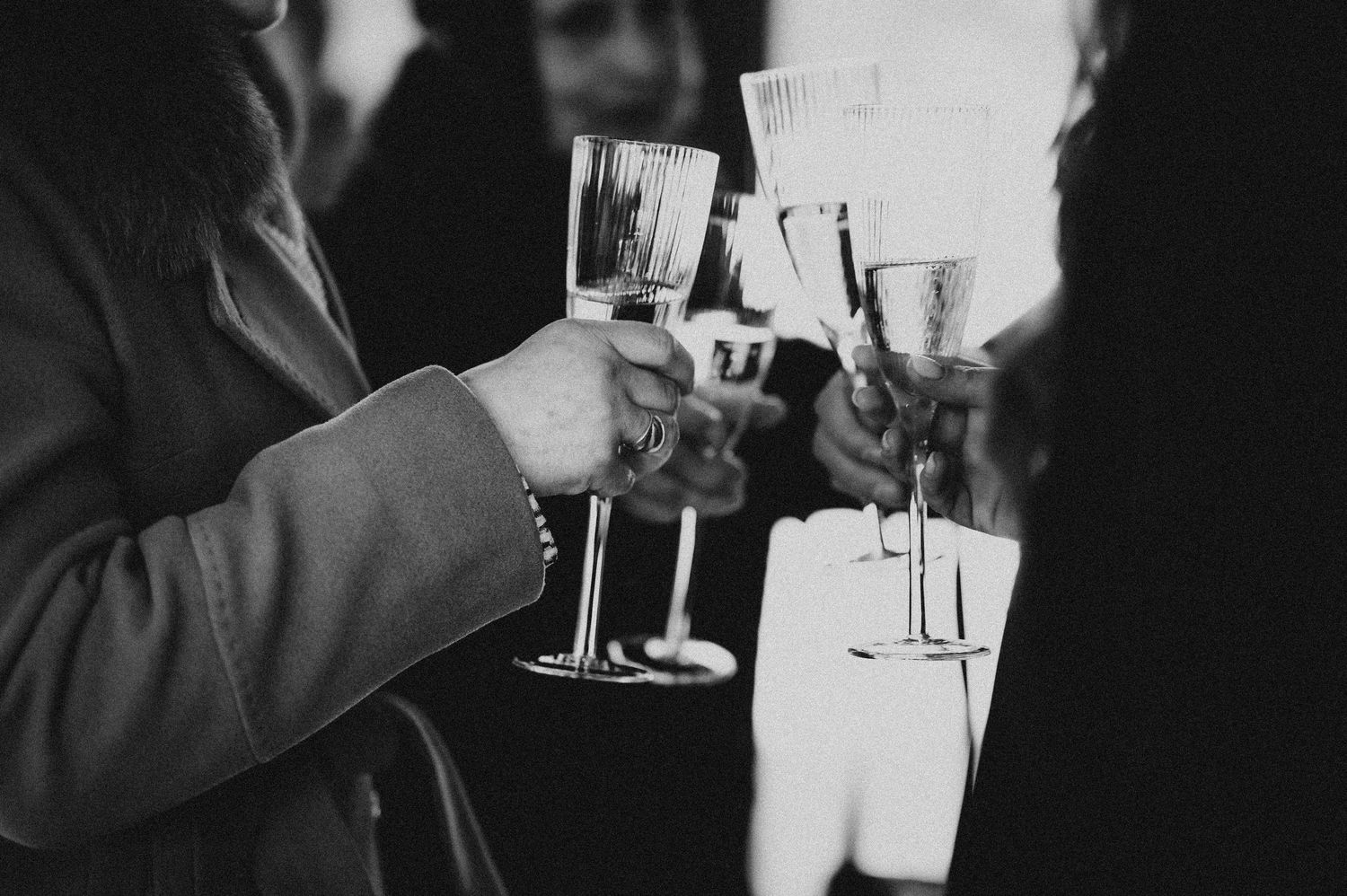 Black and white photo of guests clinking champagne glasses at an elegant celebration event.