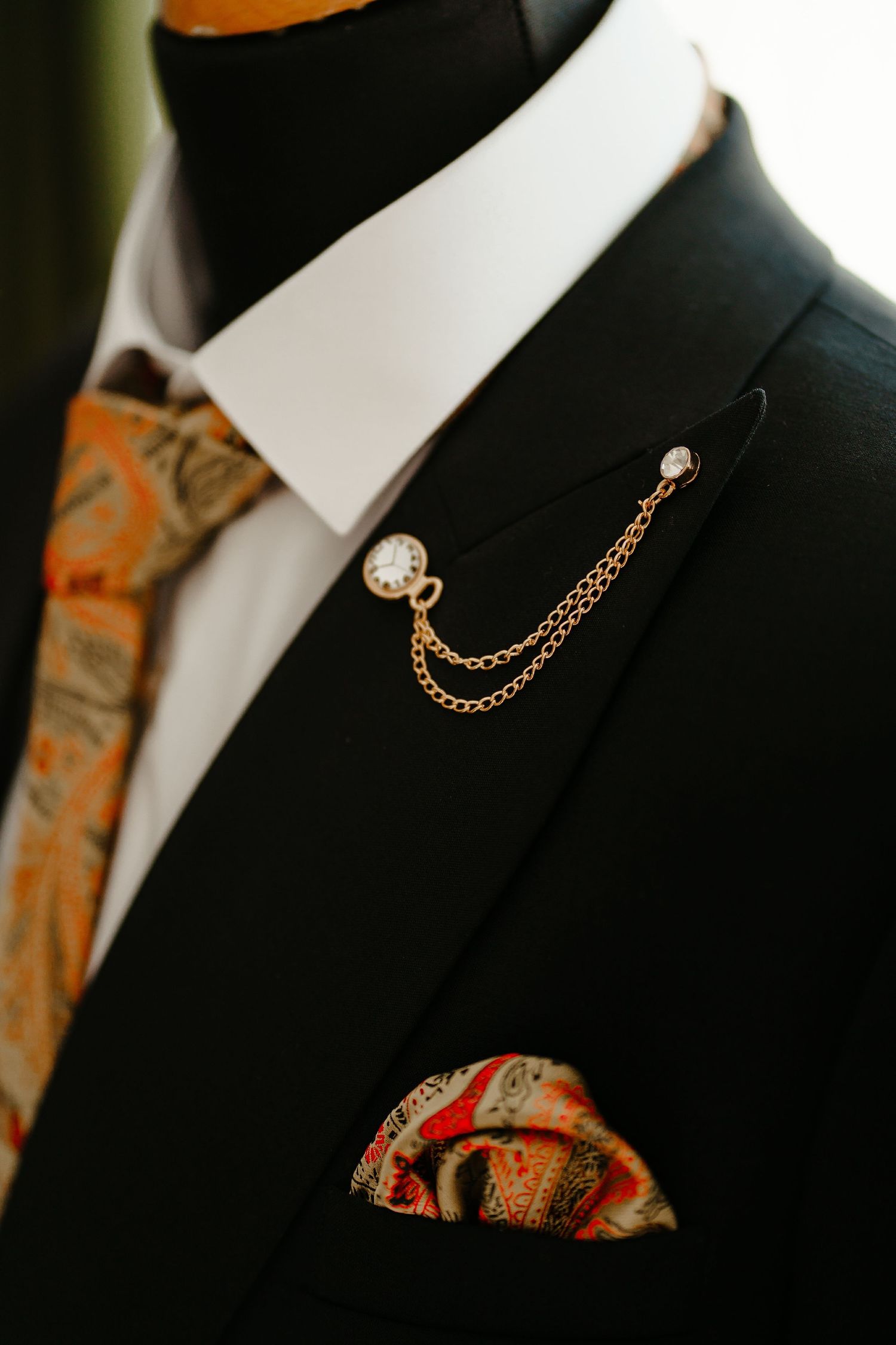 Close-up of elegant black double-breasted suit with gold chain lapel pin and paisley pocket square.