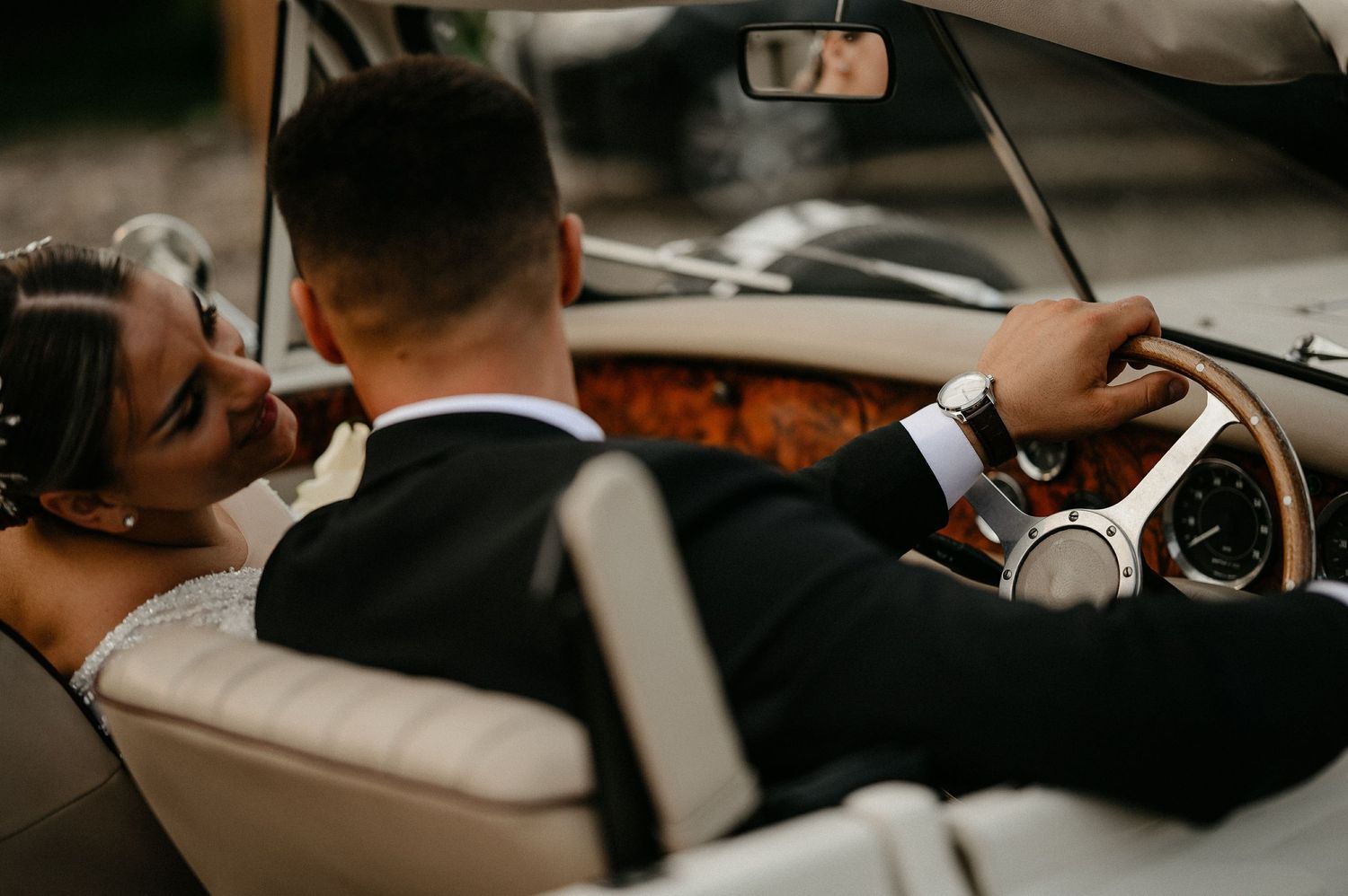 Bride and groom sharing an intimate moment in a vintage convertible car on their wedding day.