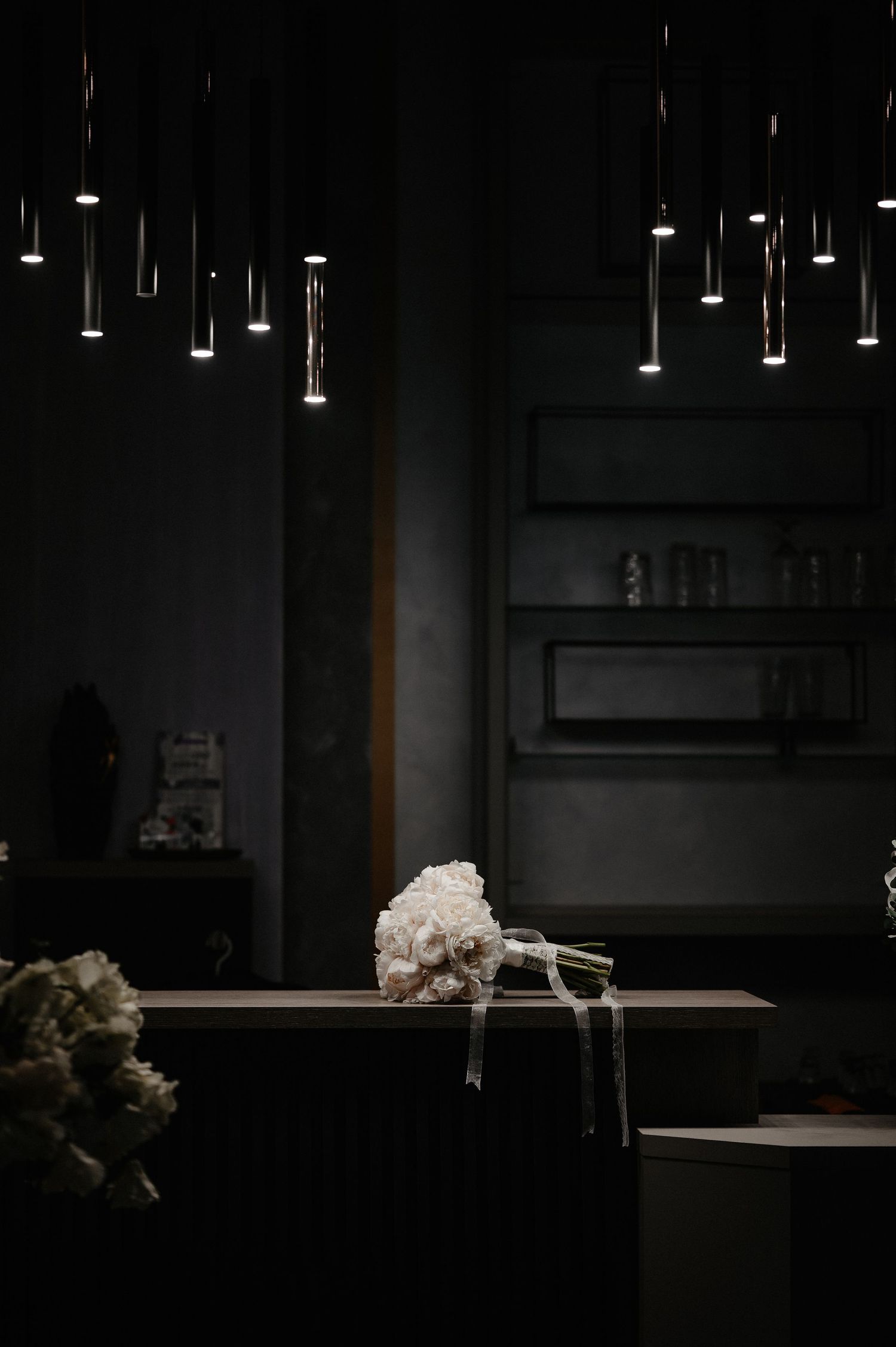 Bridal bouquet of white flowers resting on a dark counter beneath modern pendant lights.