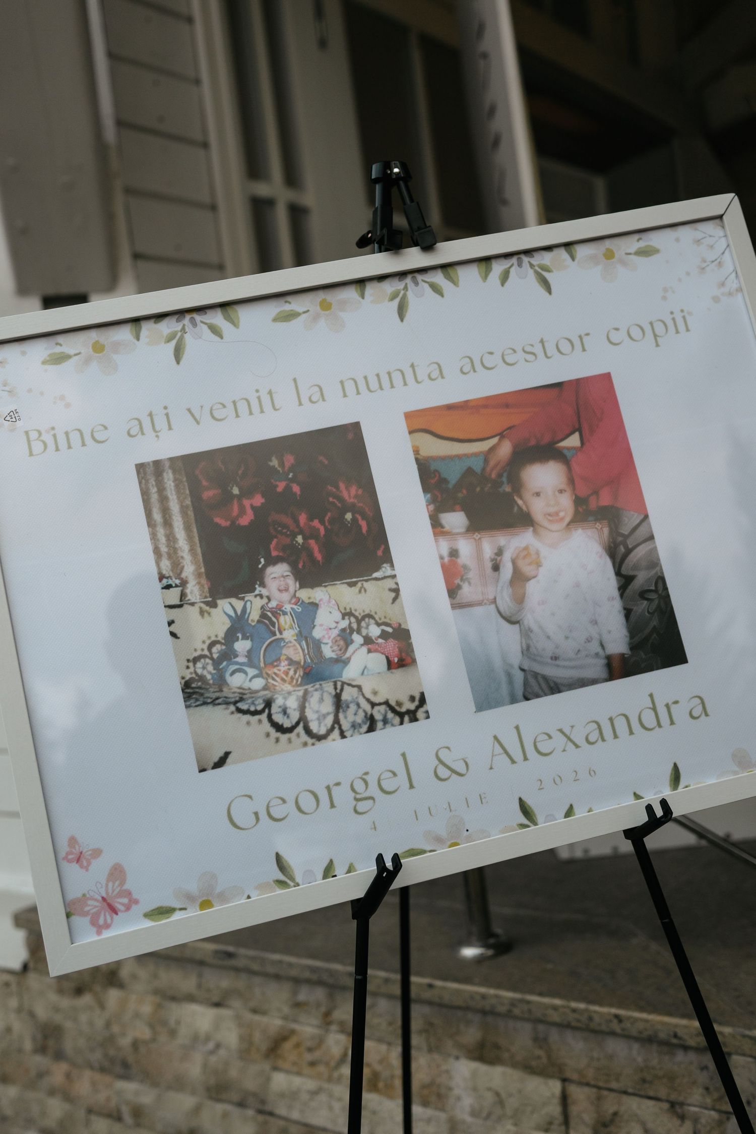 Wedding welcome sign for Georgel and Alexandra featuring childhood photos on an easel with floral decorations and Romanian text.