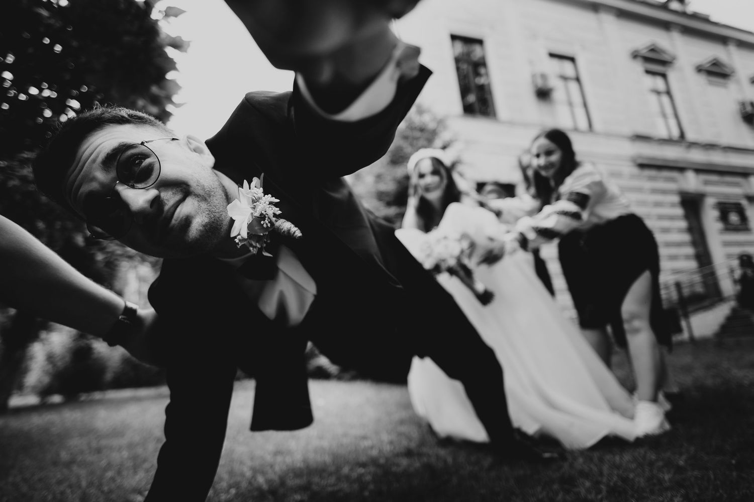 Fun black and white wedding photo of groomsman leaning with bridal party outdoors.