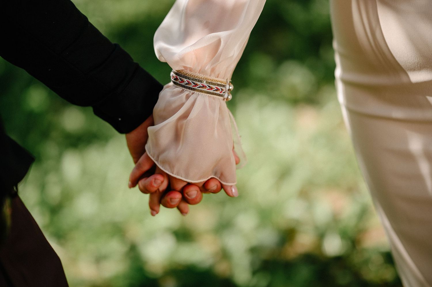 Close-up of bride and groom holding hands, bride wearing silver bracelet.
