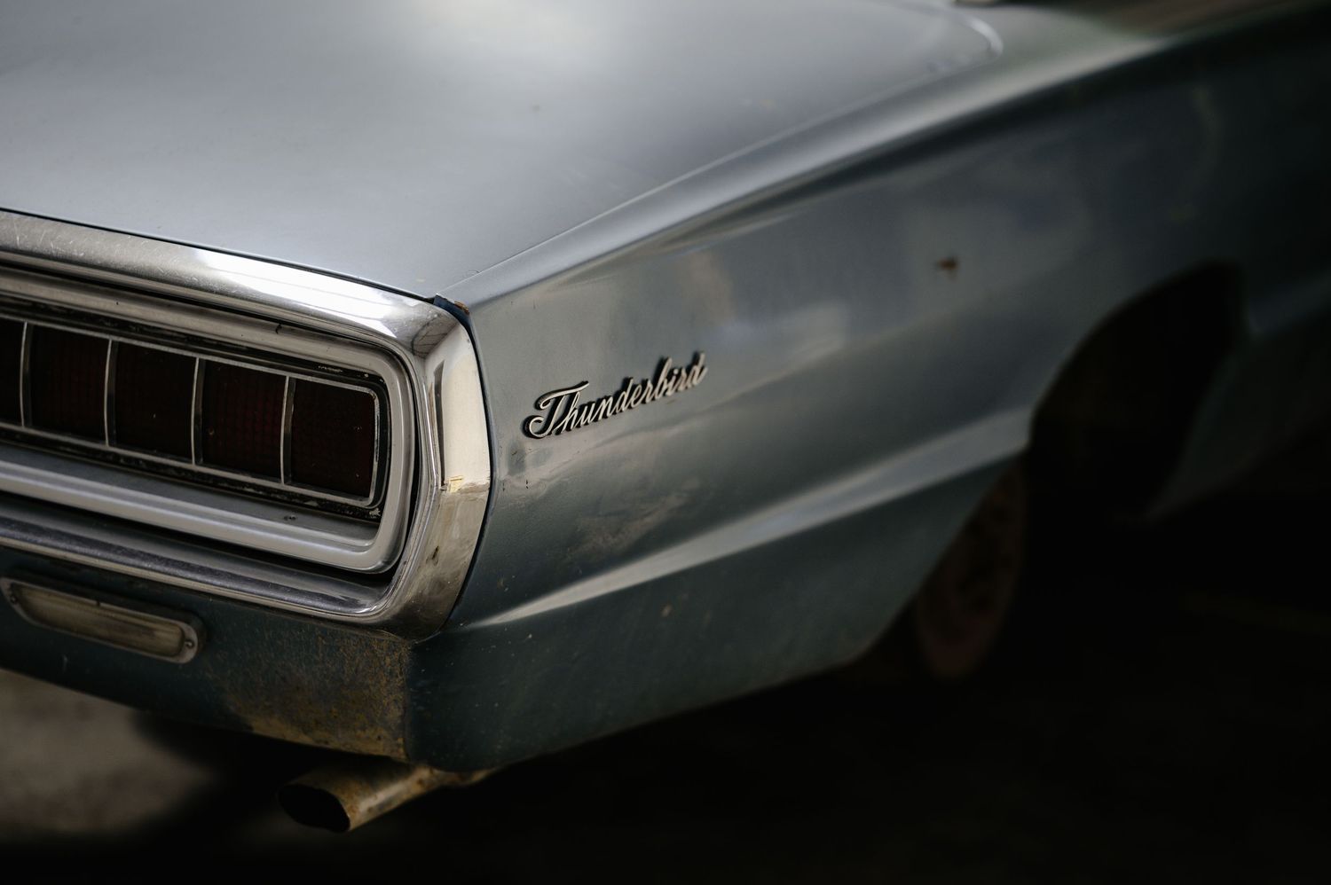 Vintage Dodge Thunderbolt muscle car in faded blue, showing rear quarter panel and tail lights in a dark setting.