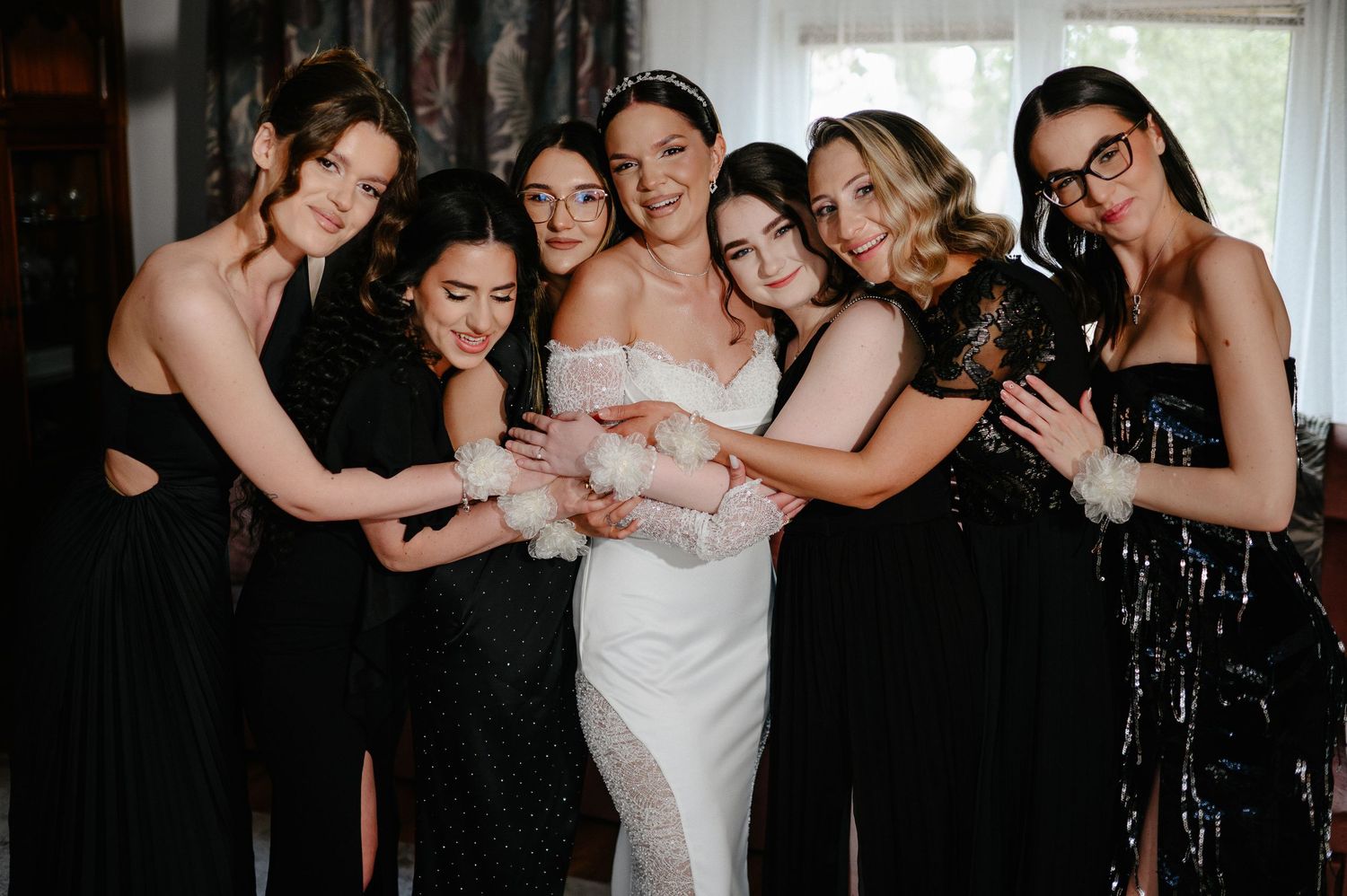 Bride surrounded by six bridesmaids in black dresses with white floral wrist corsages.