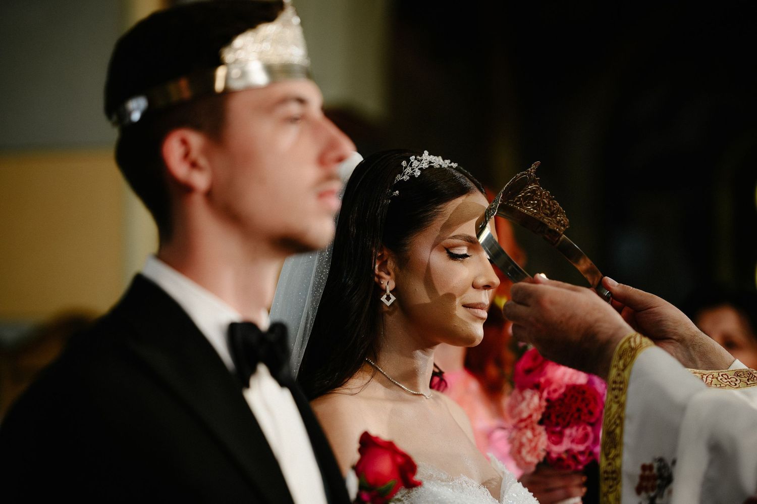 Orthodox priest anoints bride with tiara and veil during religious wedding ceremony ritual.