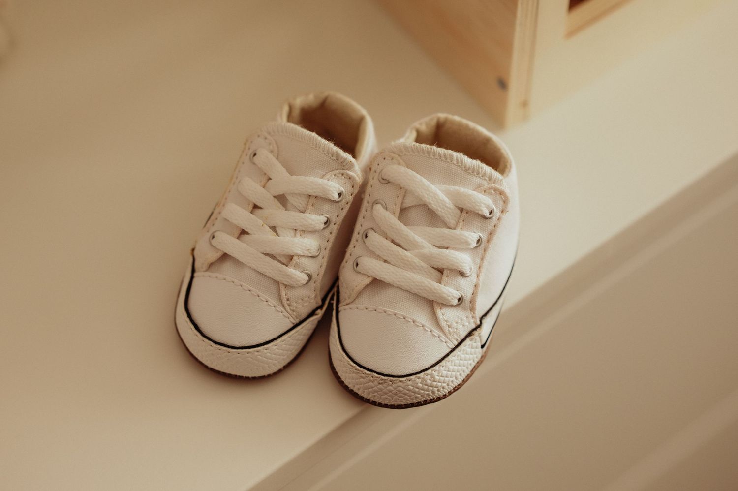 Tiny white Converse Chuck Taylor baby sneakers placed on a light-colored surface.