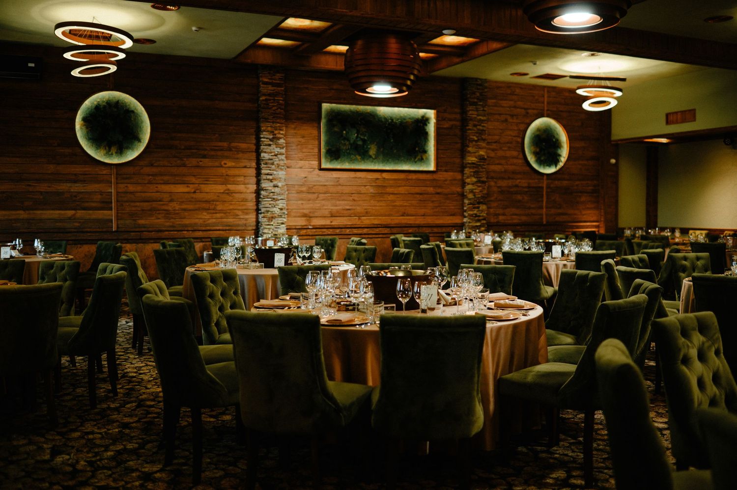 Elegant dark wood wedding reception hall with round tables and green velvet chairs.