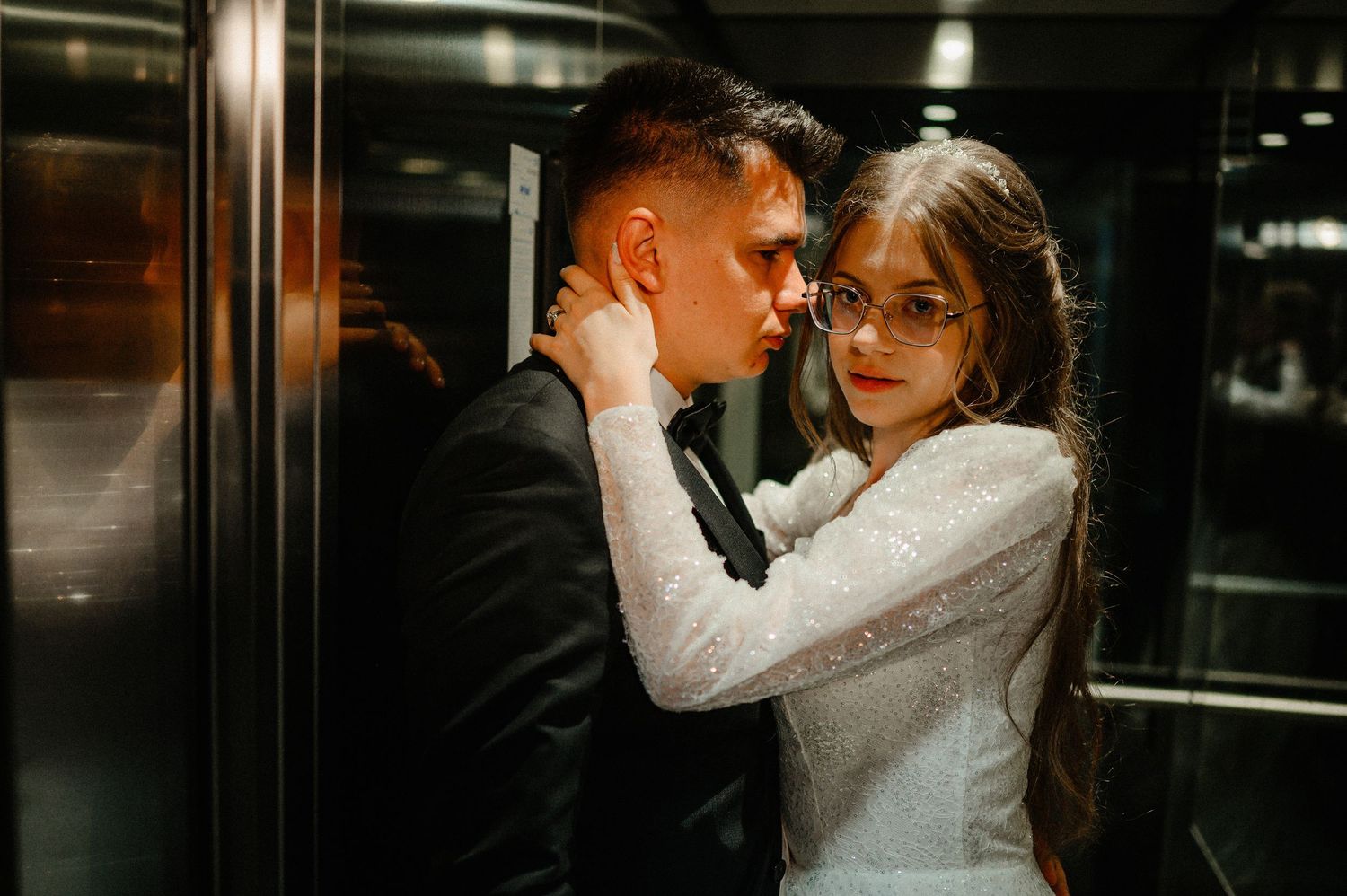 Bride and groom share an intimate embrace in a modern elevator on their wedding day.