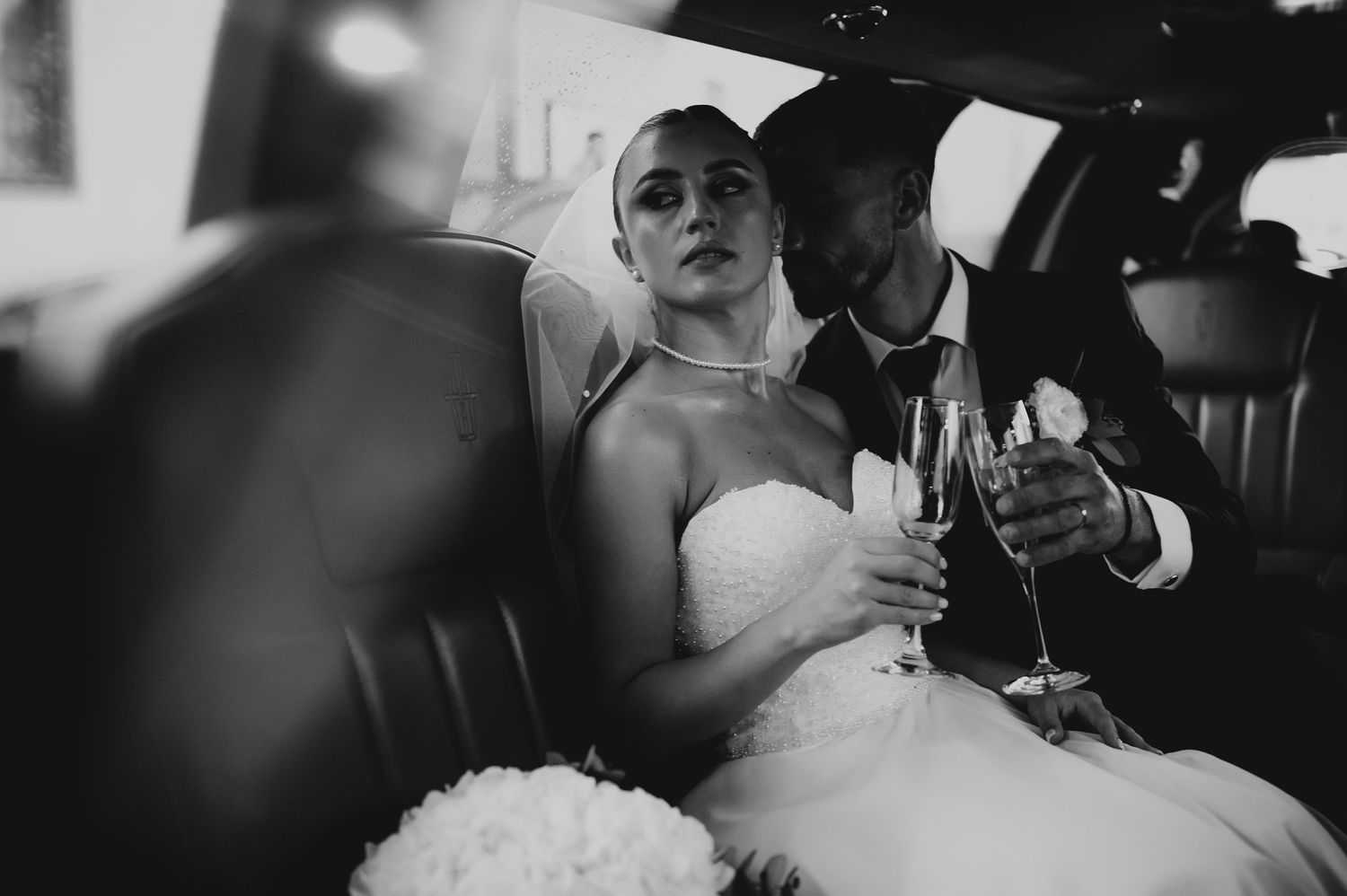 Black and white photo of bride and groom toasting with champagne glasses inside a limousine.