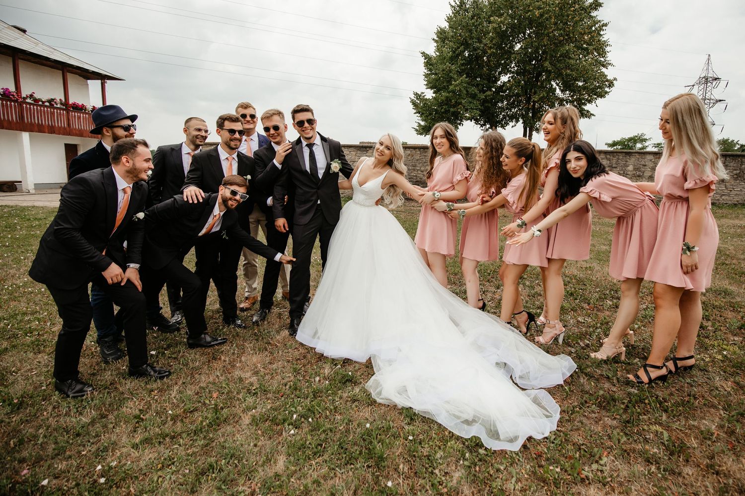 Wedding party with groomsmen in suits and bridesmaids in pink dresses celebrating with bride and groom outdoors.