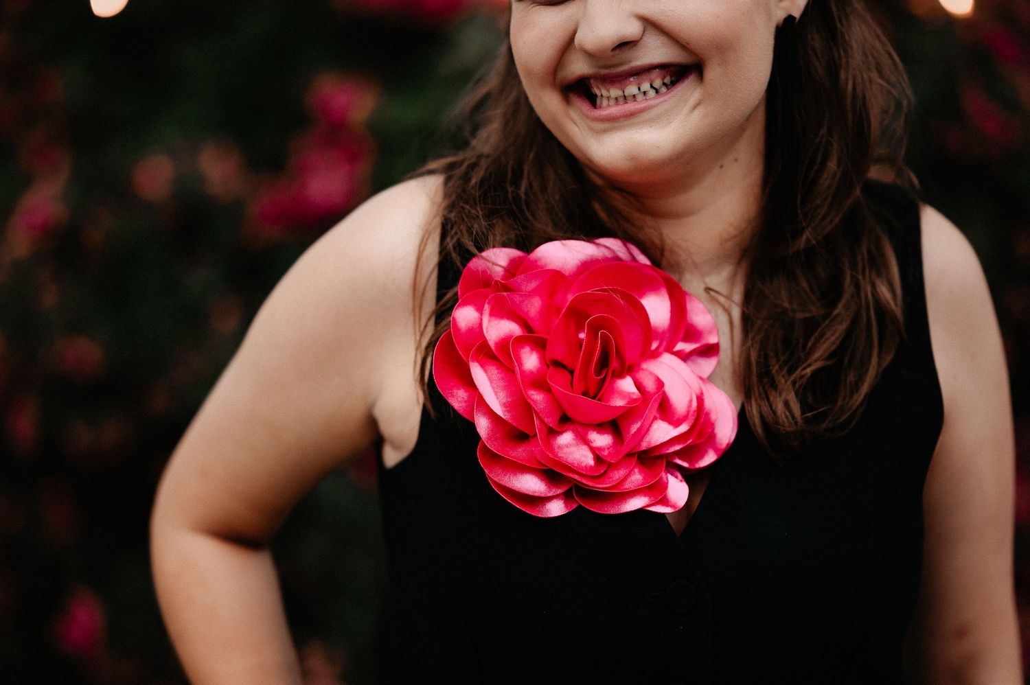 Laughing young woman in black dress wearing large pink rose corsage at outdoor celebration event.